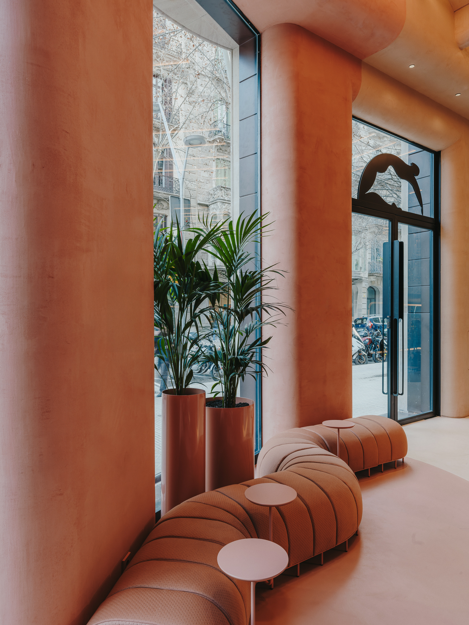 Corner window detail with potted palms and segmented lounge seating beneath arched ceiling