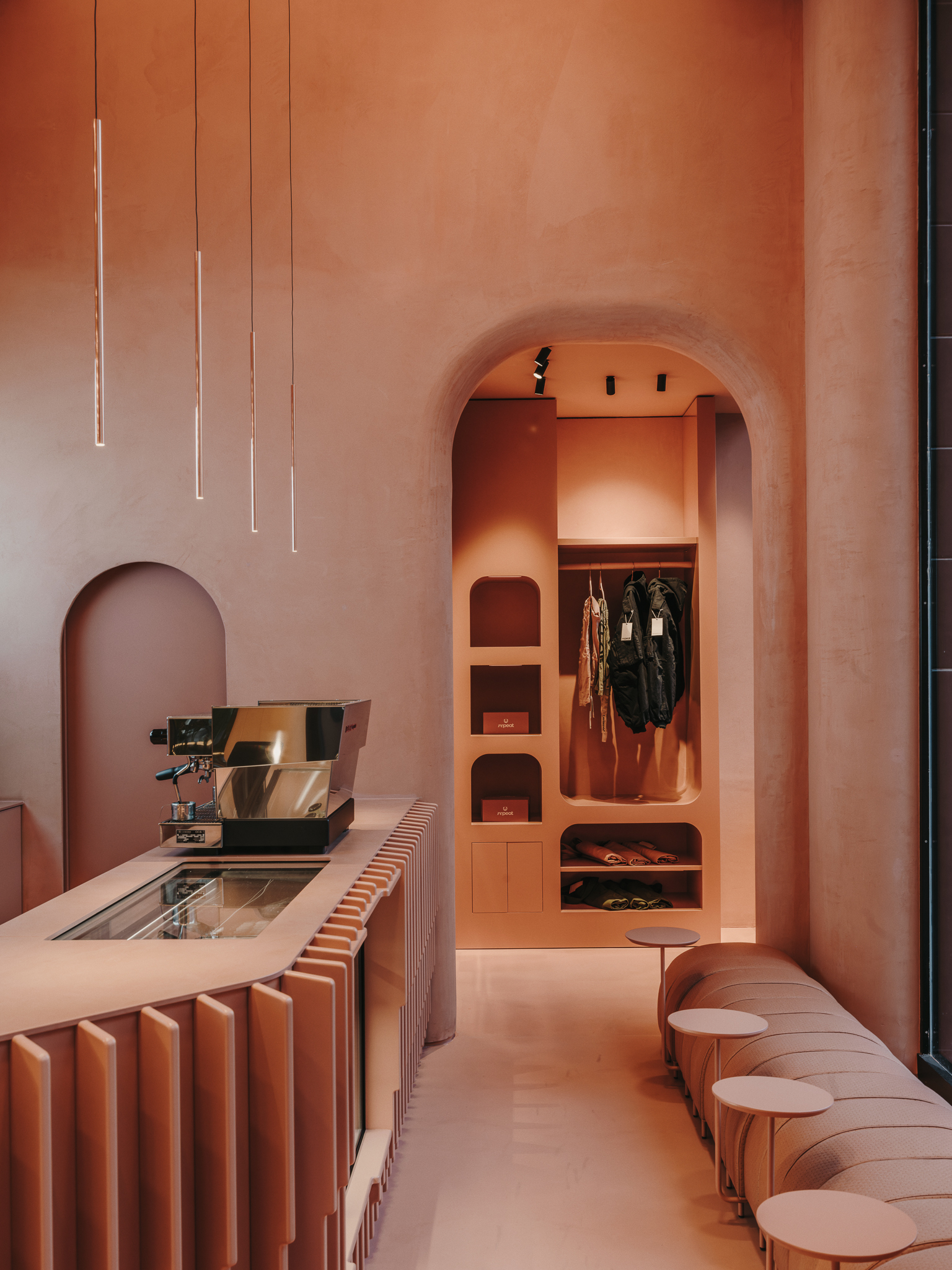 Espresso bar counter with vertical pendant lights and an arched alcove displaying retail items