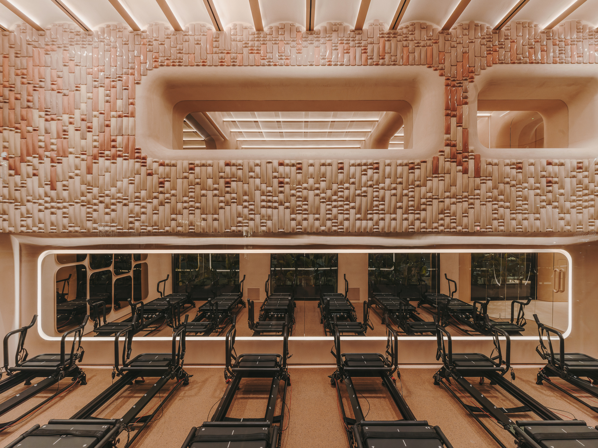 Frontal view of the textured basketweave wall with recessed openings and Pilates reformers on lower level