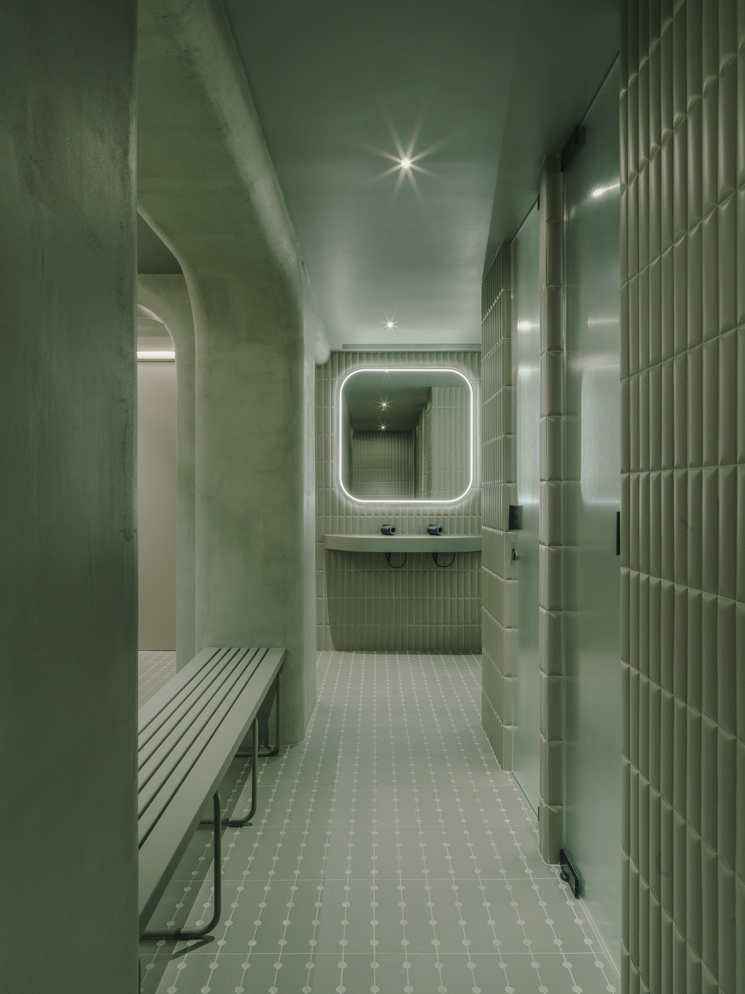 Locker room corridor with ribbed green tile walls, white mosaic floor and backlit mirror