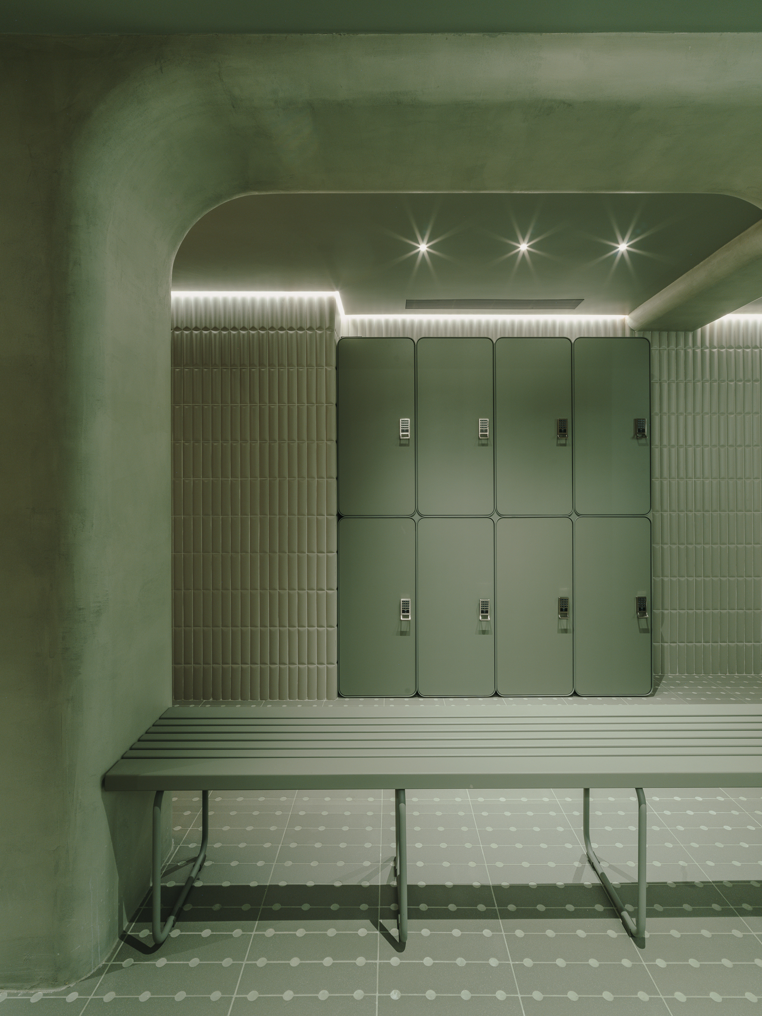 Locker alcove with slatted bench, ribbed tile walls and recessed linear lighting above