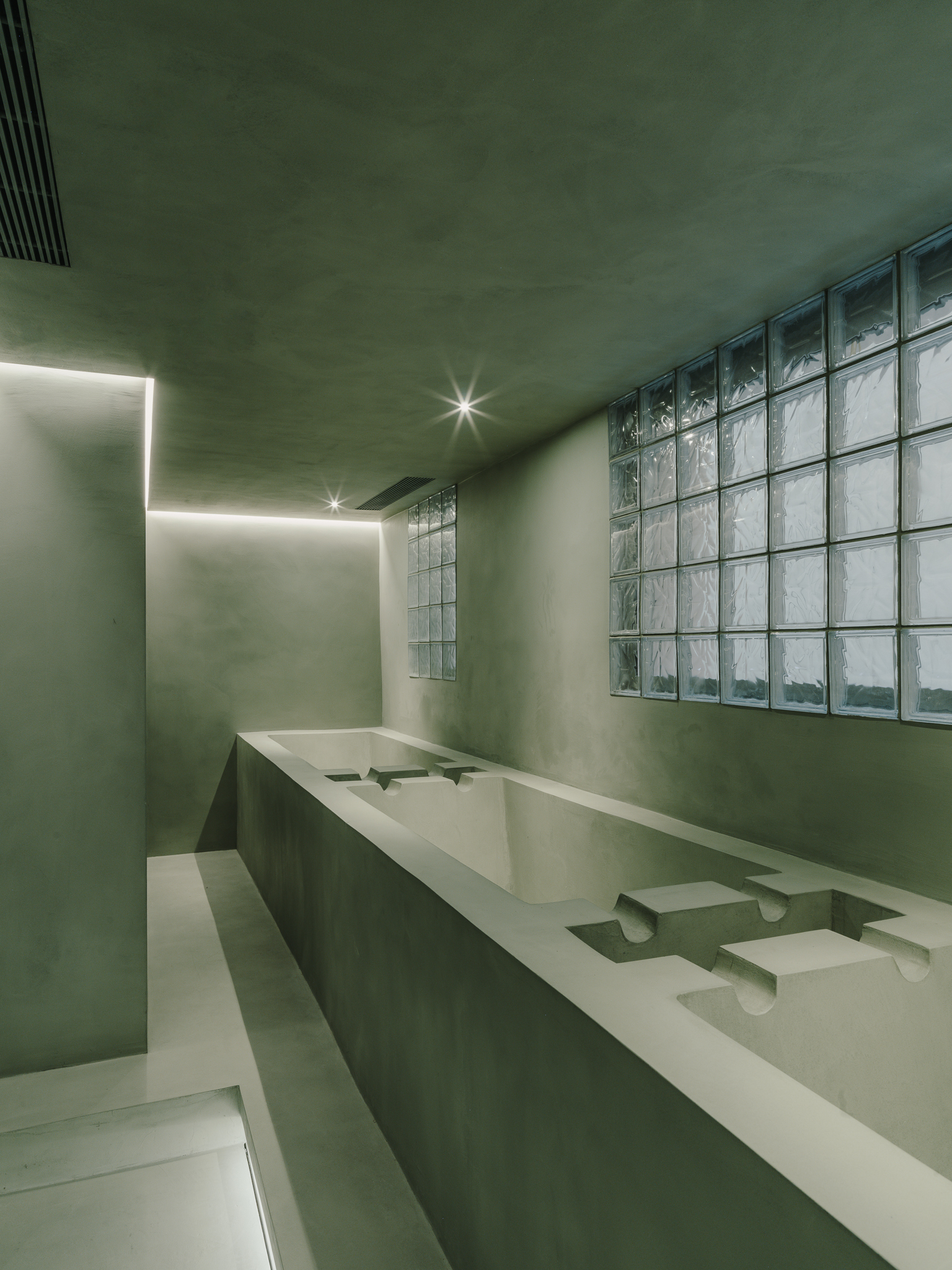 Washroom with integrated basin counter, glass block window wall and concealed ceiling lighting