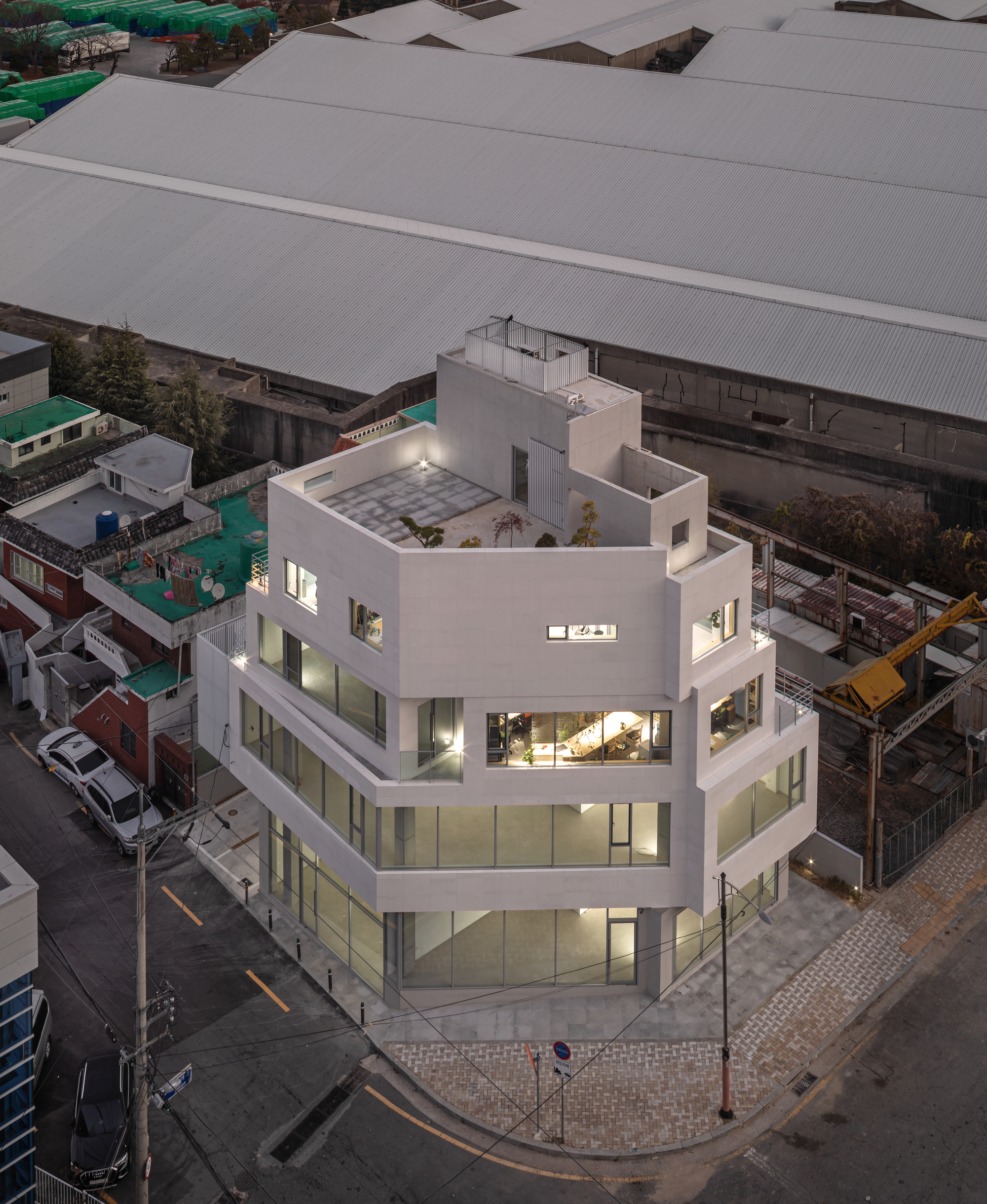 Aerial view of the corner building at dusk showing rooftop terrace and surrounding industrial sheds