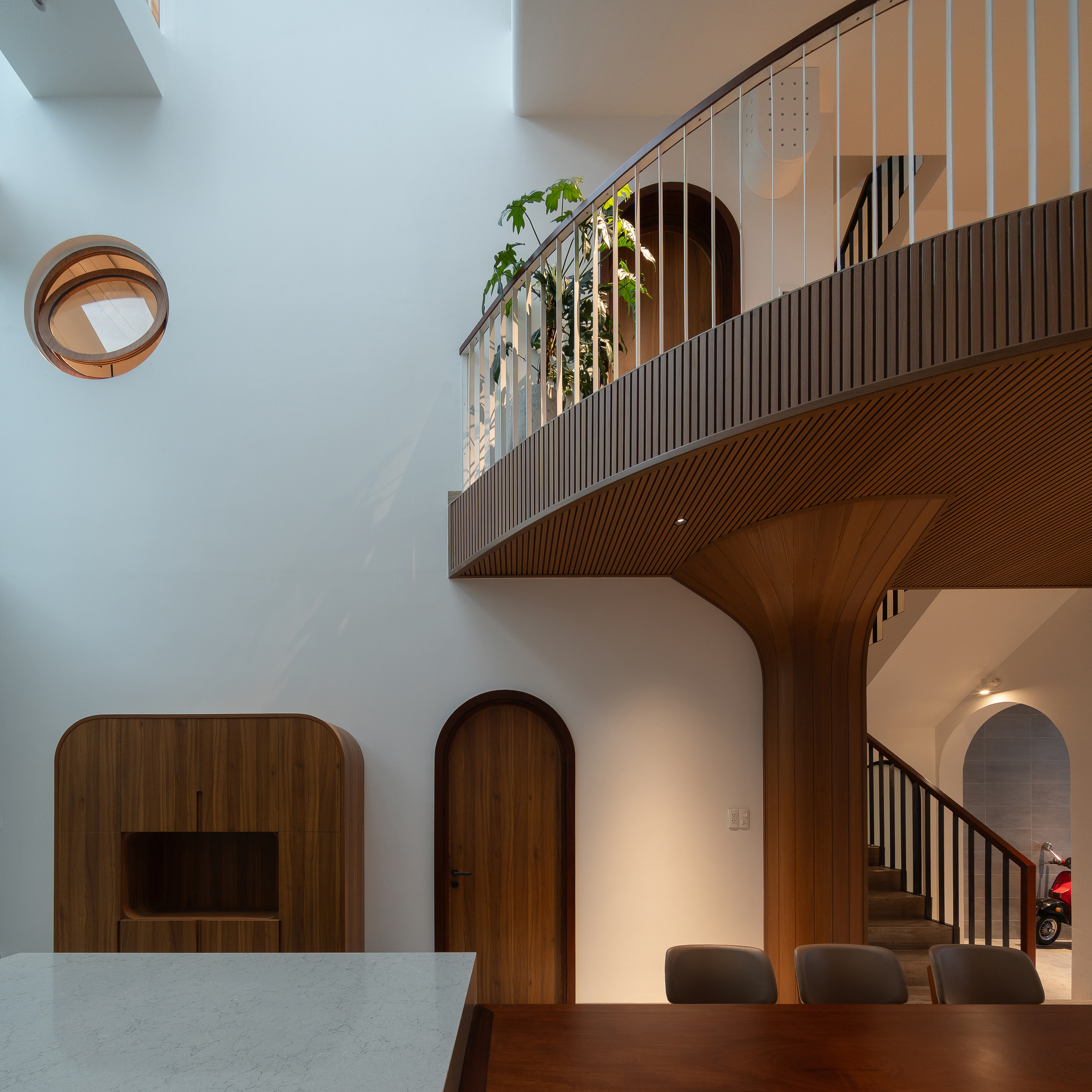 Curved timber balcony with vertical slat cladding suspended above arched doorways and dining area