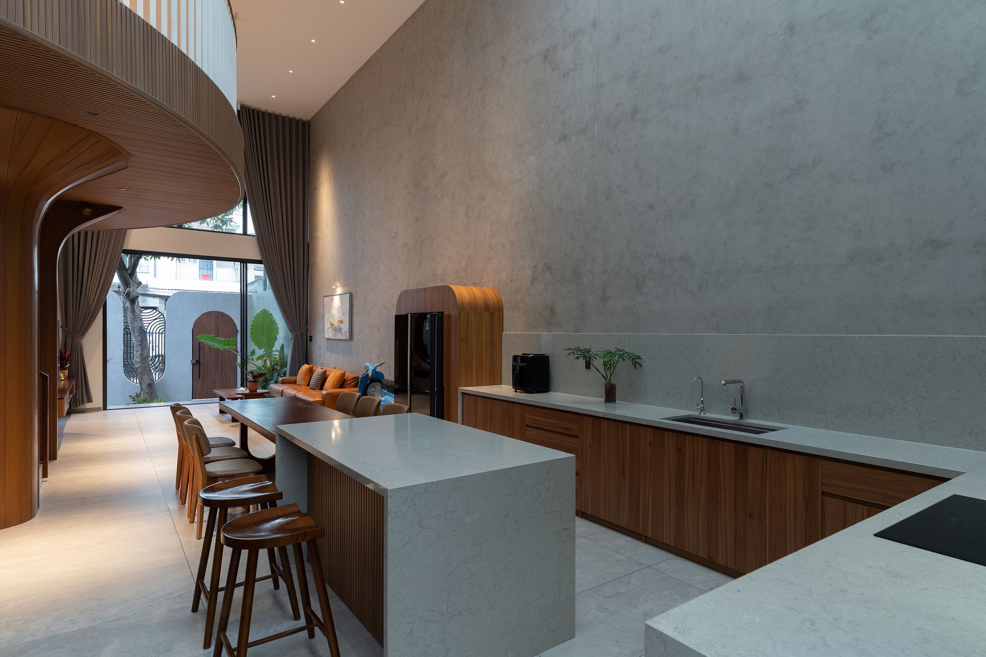 Open kitchen with marble waterfall island looking toward arched windows and planted courtyard at dusk