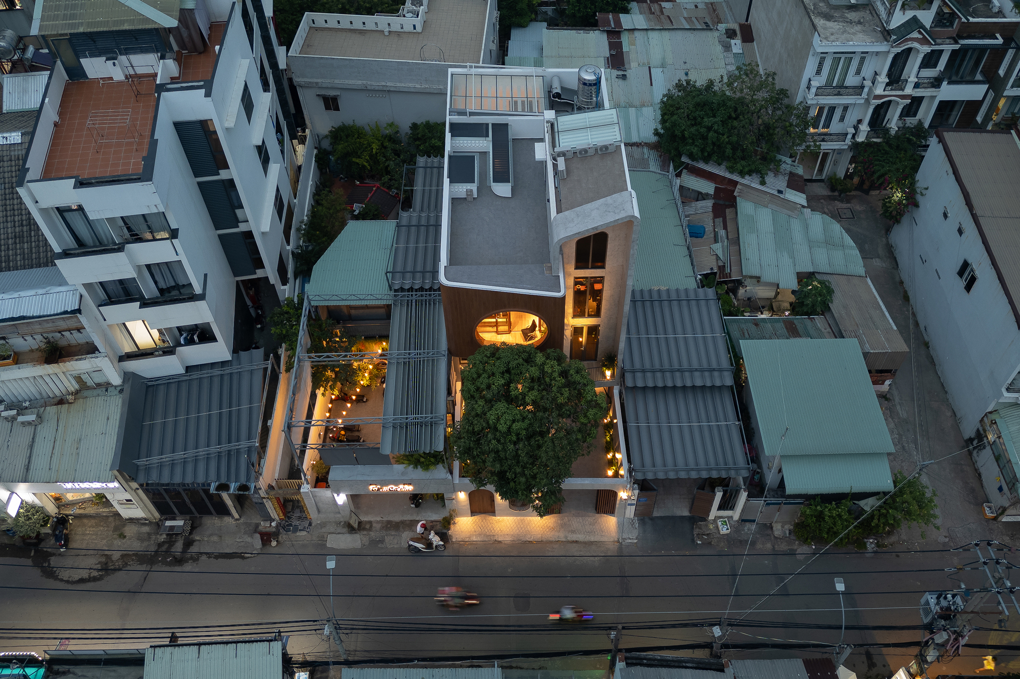 Aerial view at dusk showing the narrow house wedged between neighboring structures with interior lights glowing
