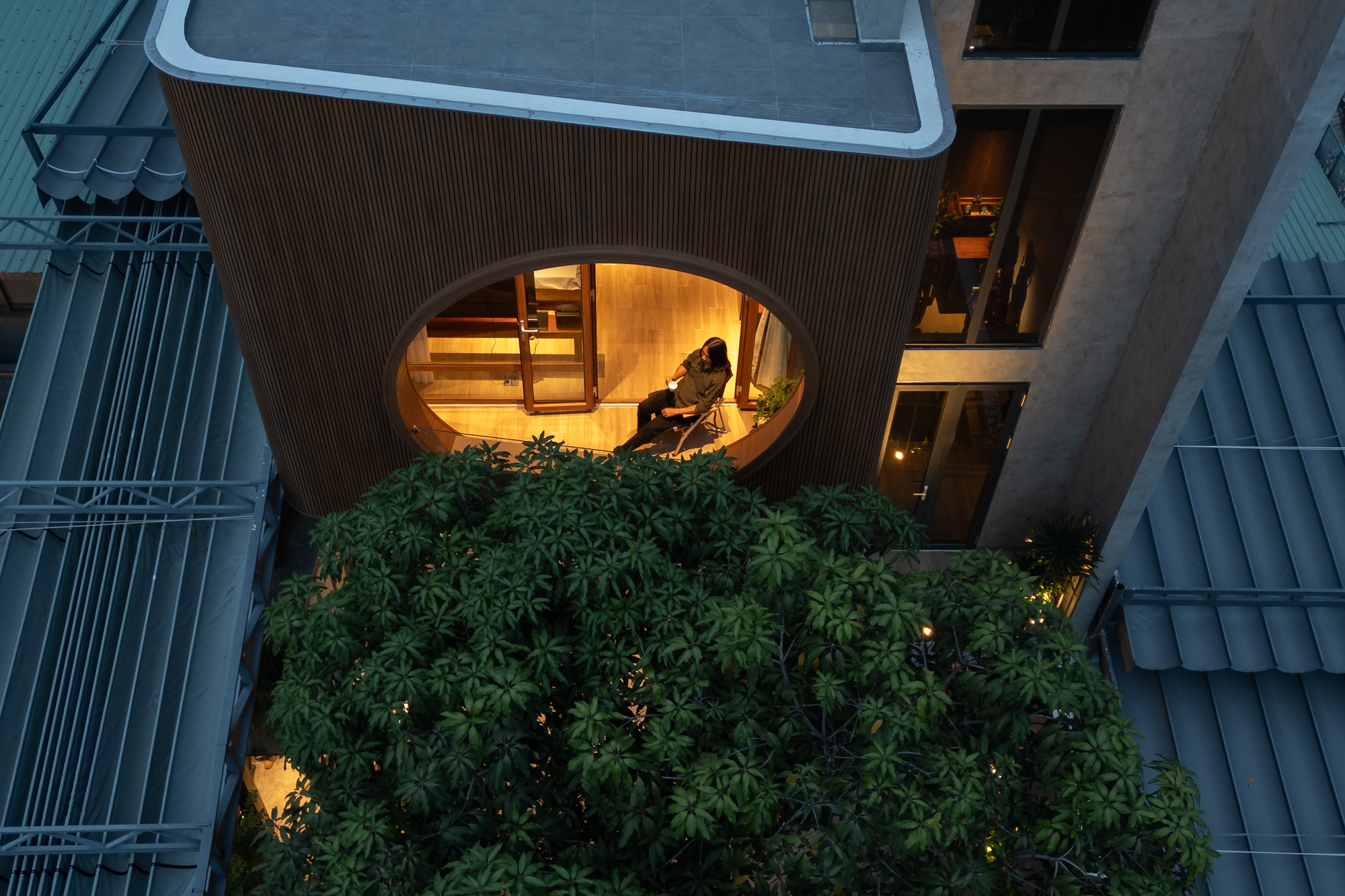 Overhead view of the circular terrace window with a figure seated inside above dense green planting