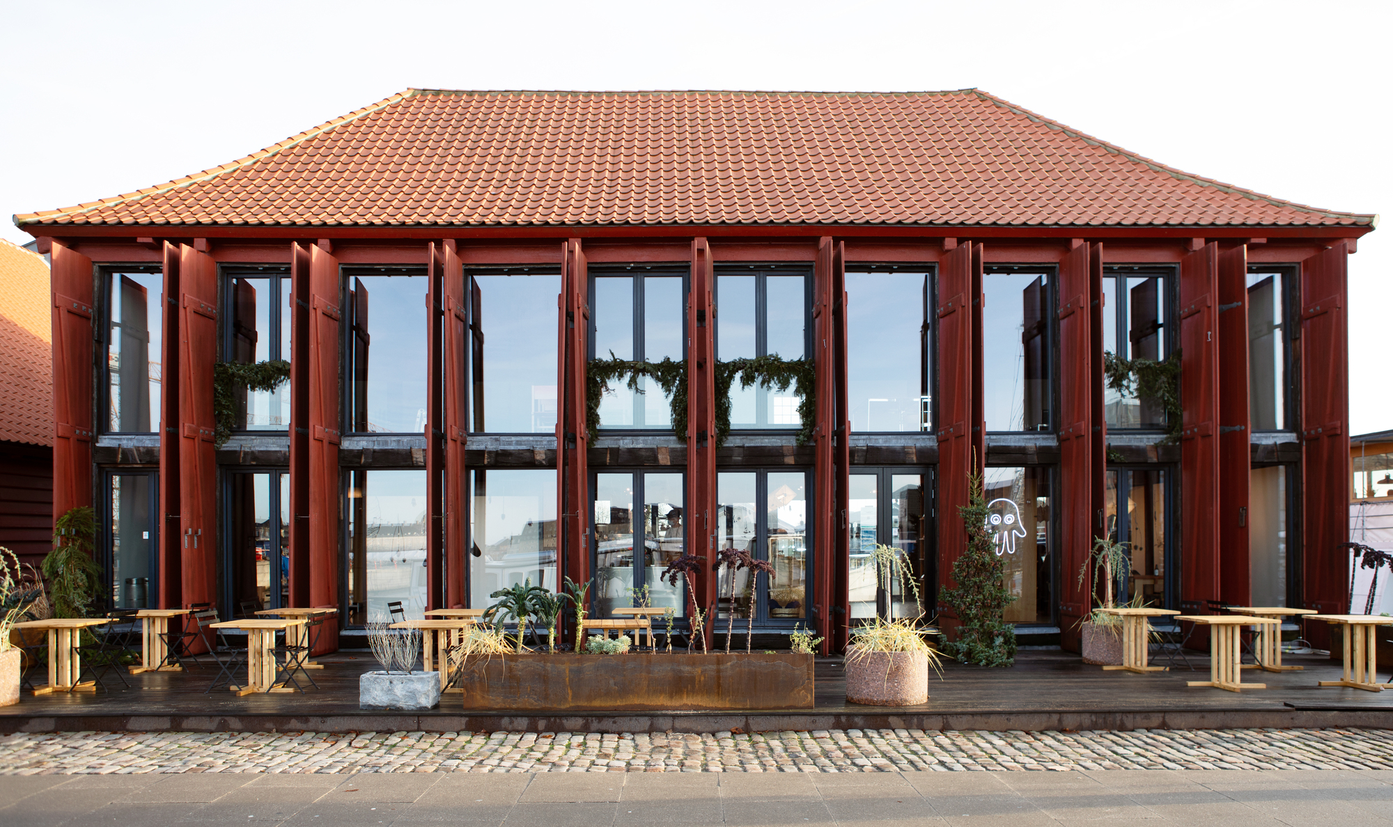 Street facade with red-tiled hip roof, gridded glass doors, and timber benches on a paved plaza