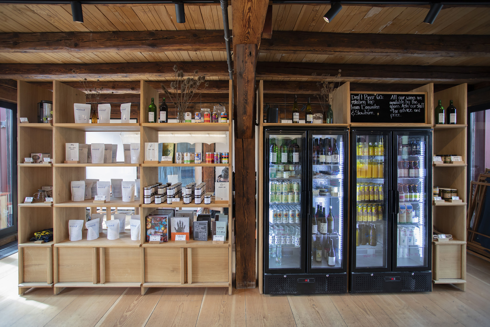 Retail wall with open timber shelving and glass-door refrigerators flanking a dark timber column