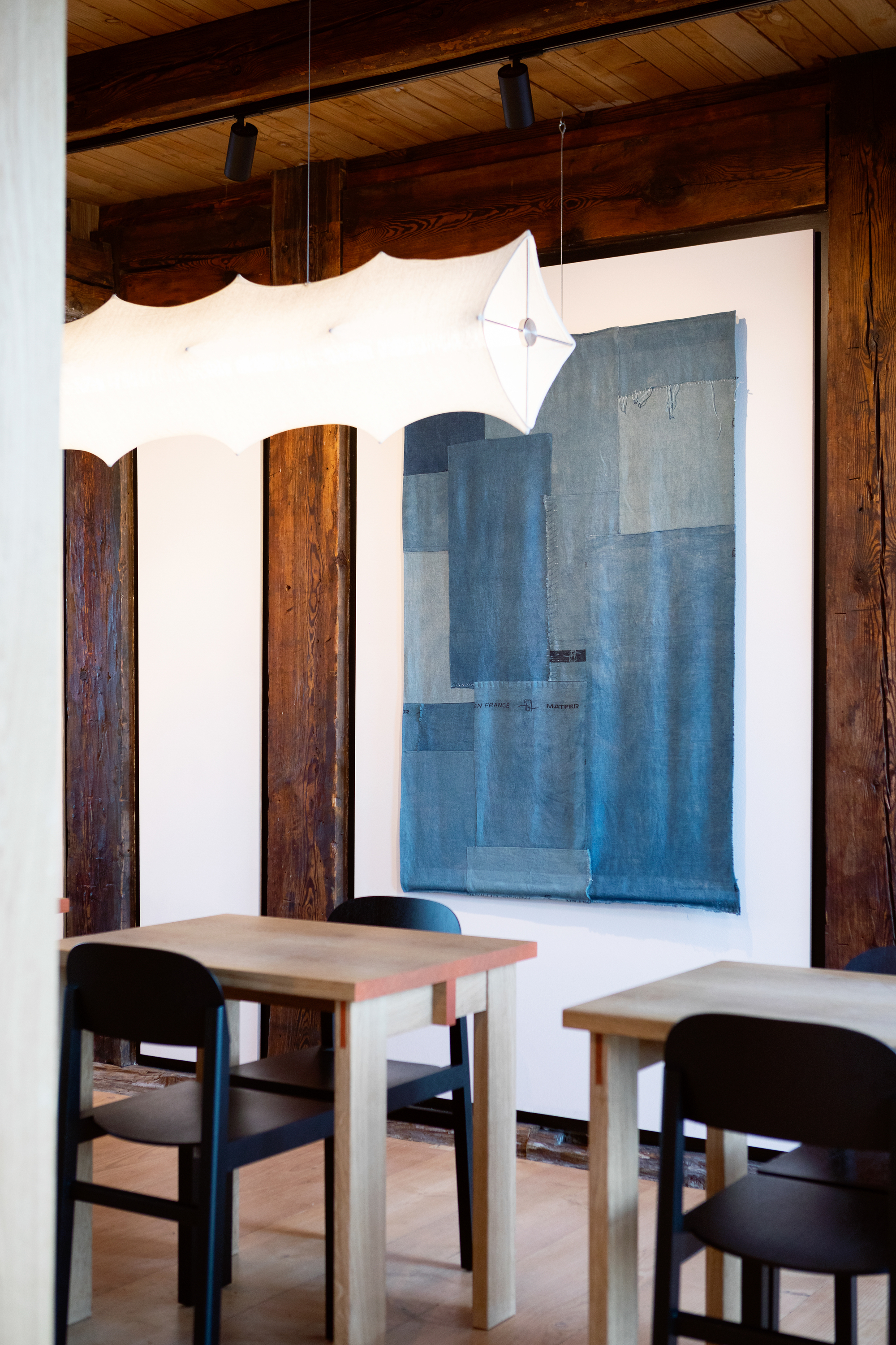 Interior seating with timber tables, black chairs, and a textile hanging between exposed wood columns