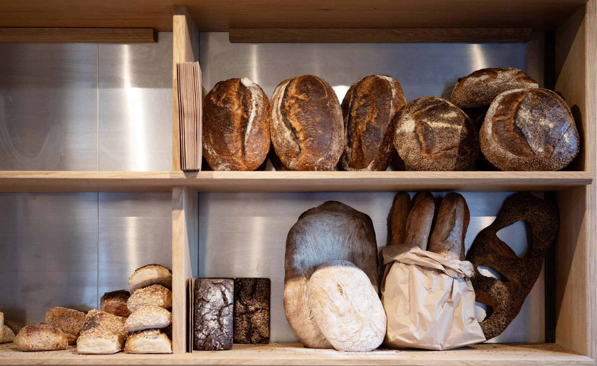 Open shelving unit displaying artisan bread loaves with stainless steel backsplash and integrated strip lighting