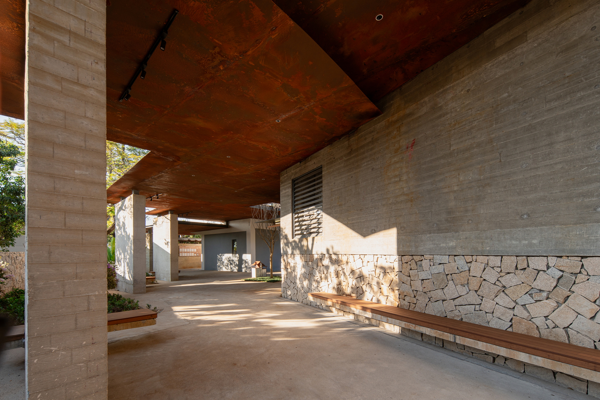 Covered walkway with weathered steel ceiling and stone and brick walls in afternoon light