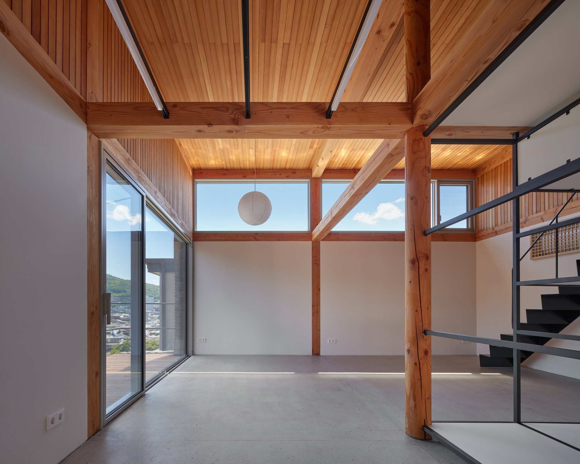 Double-height interior with exposed timber beams and columns framing glazed walls overlooking the surrounding rooftops