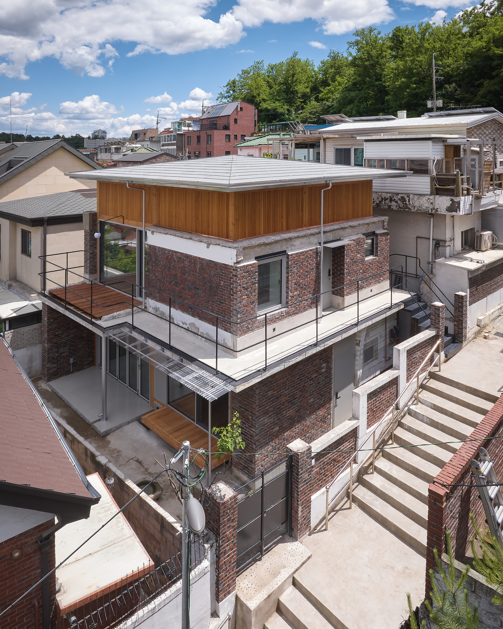 Elevated view of the three-story brick volume with timber-clad roof and steel-railed terraces under a partly cloudy sky