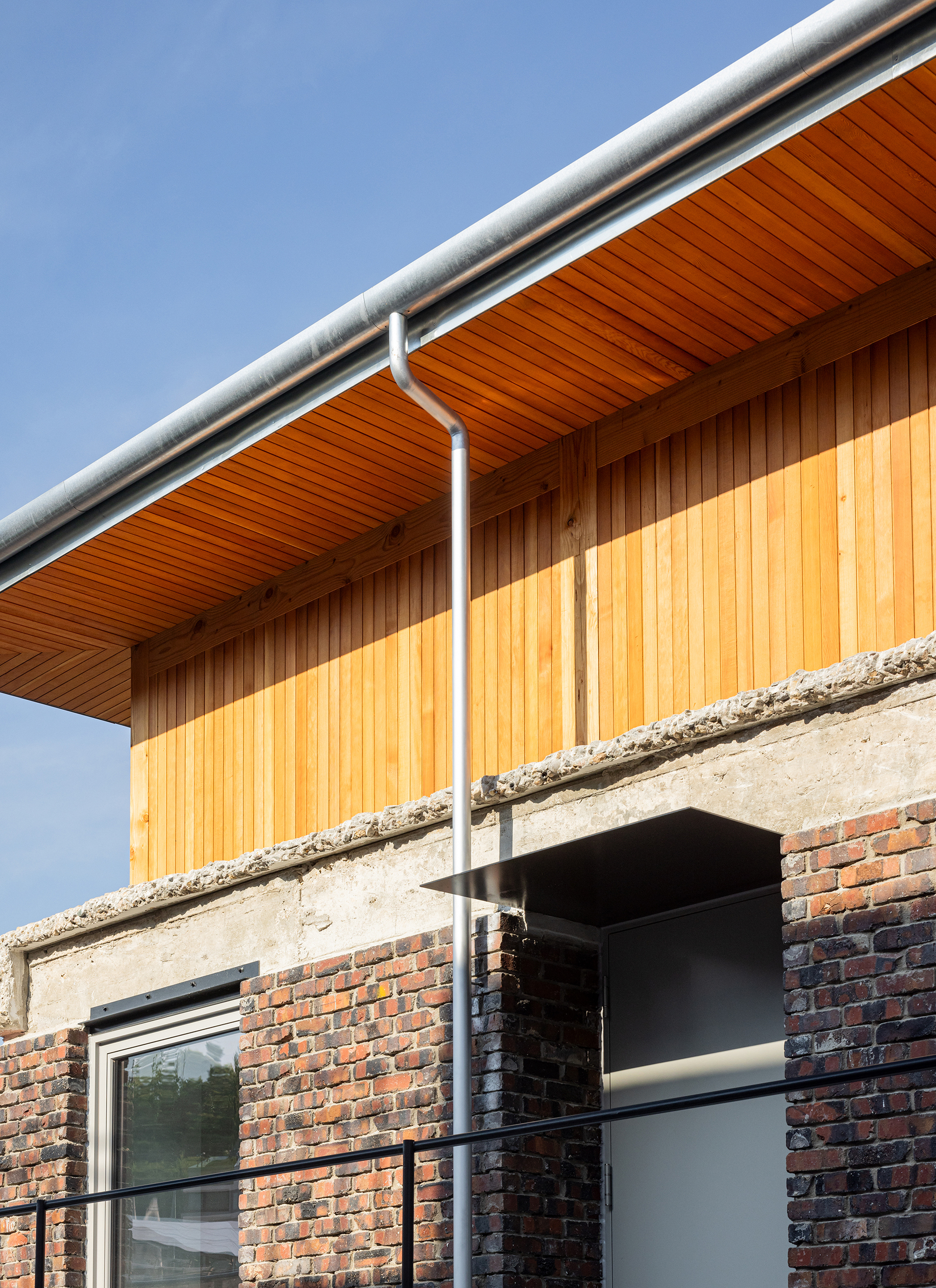 Upper level timber-clad addition with exposed soffit and white gutter above original brick facade
