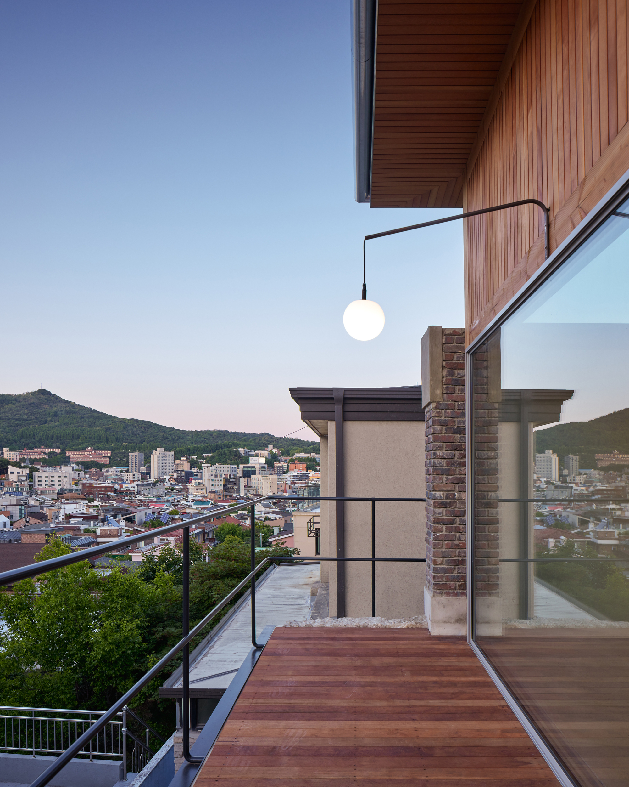 Roof terrace with timber decking and glass balustrade overlooking hillside neighborhood at dusk
