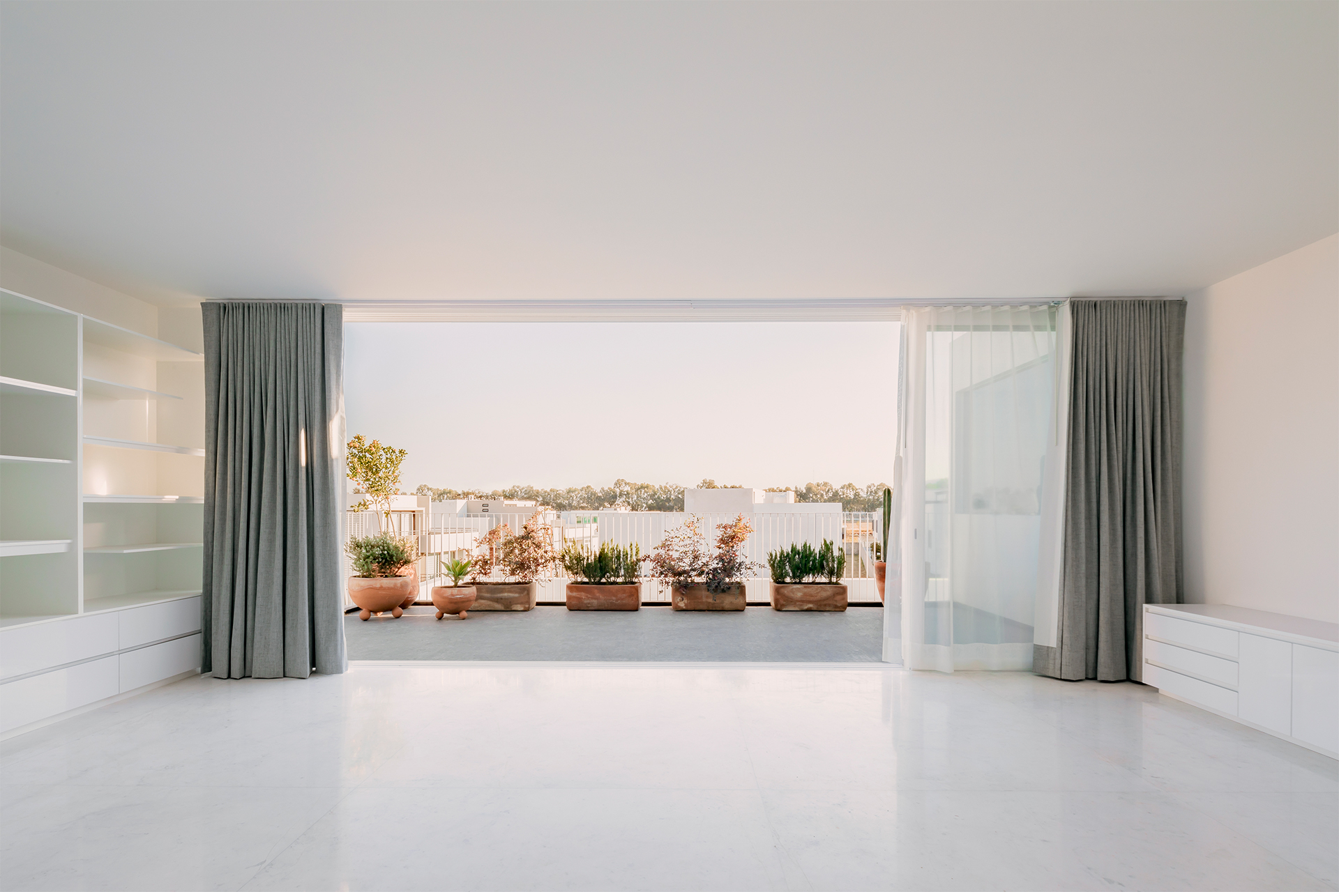 Interior room with built-in shelving opening to a terrace lined with terracotta planters