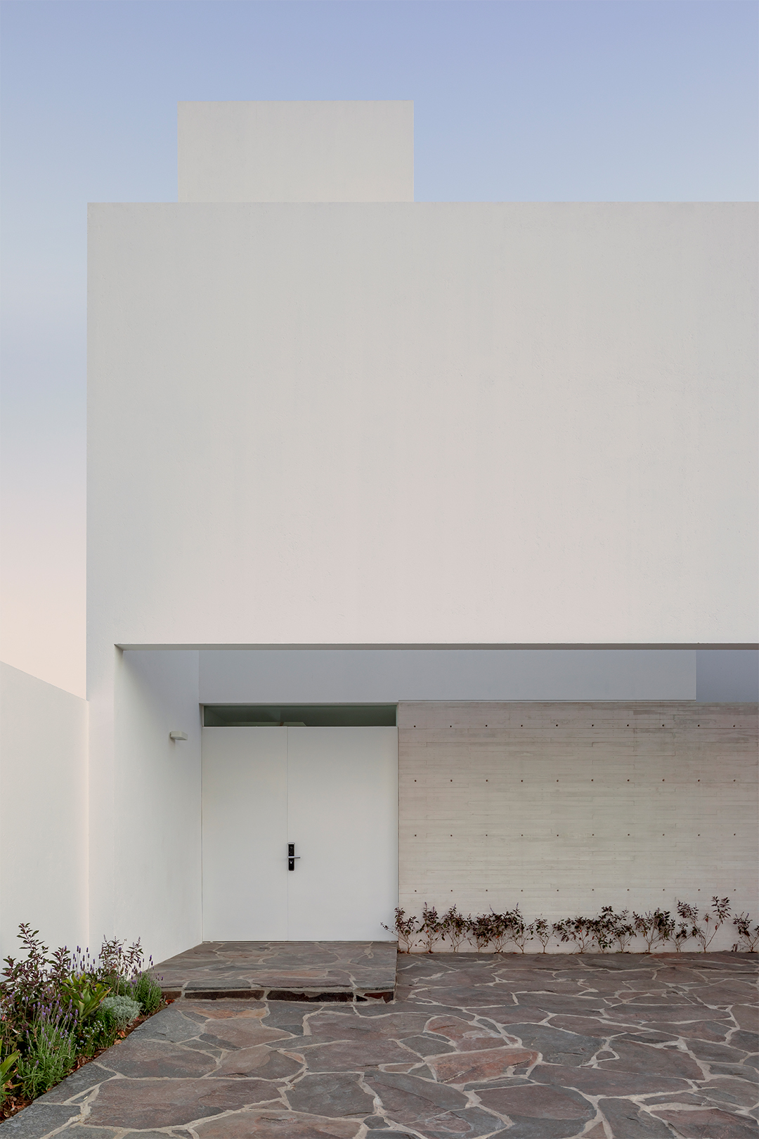 Entry canopy sheltering a concrete platform and board-formed wall at dusk