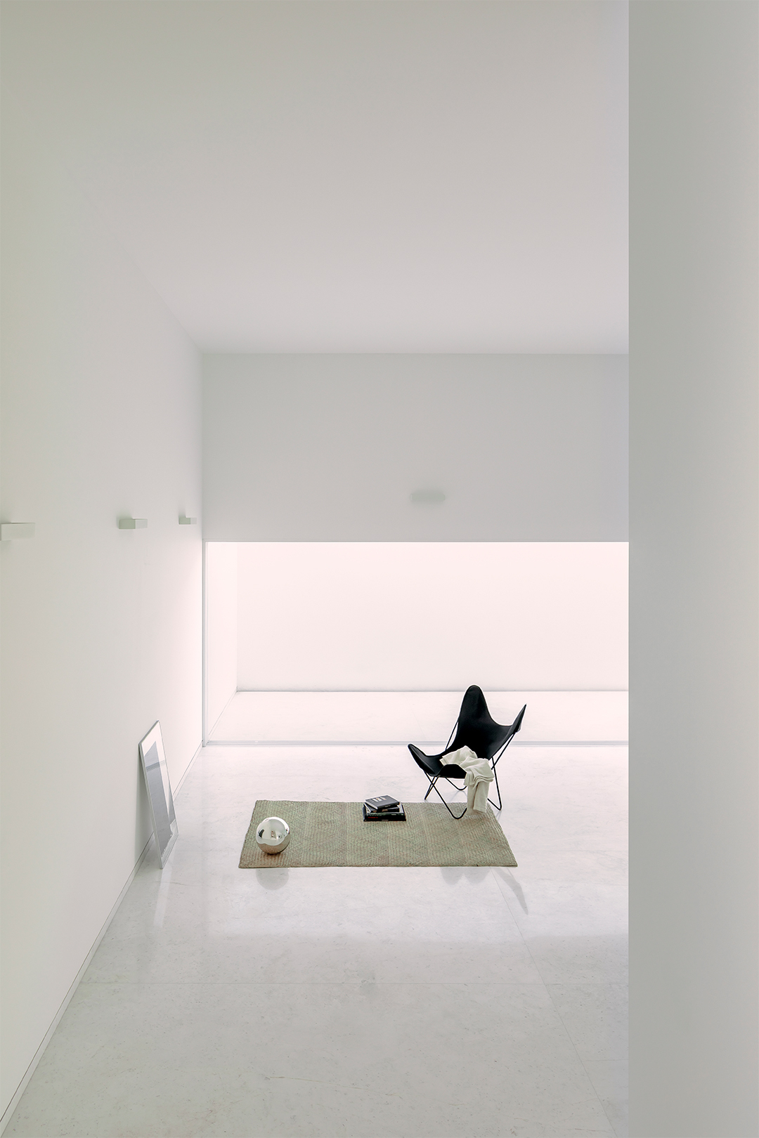 Framed view through doorway to a butterfly chair on a woven rug beneath a horizontal window