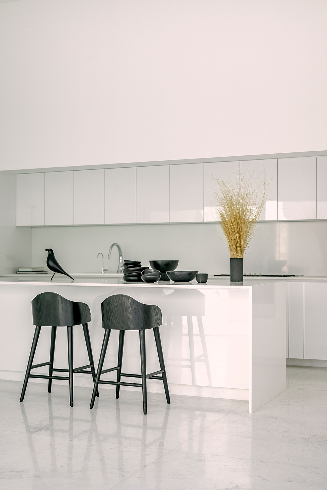 Kitchen island with black bar stools and decorative wheat stems against white cabinetry and terrazzo floor