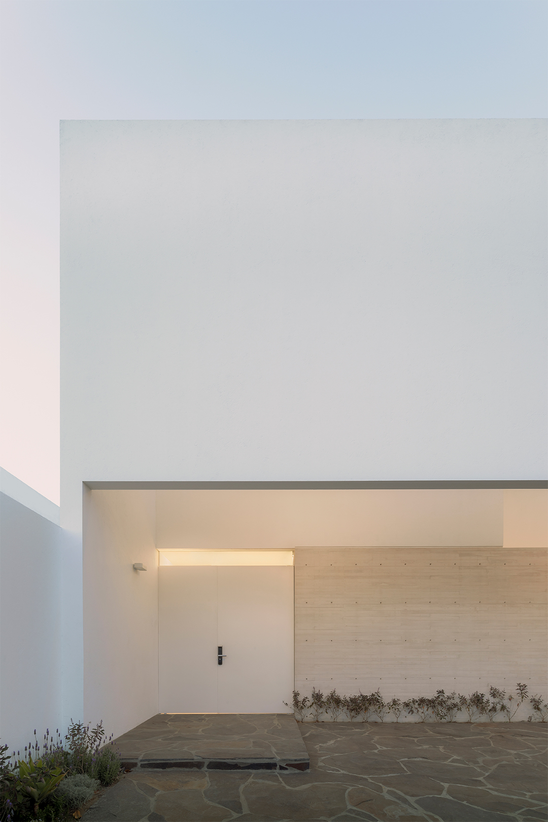 Covered entry courtyard with timber-clad wall and irregular stone paving at twilight
