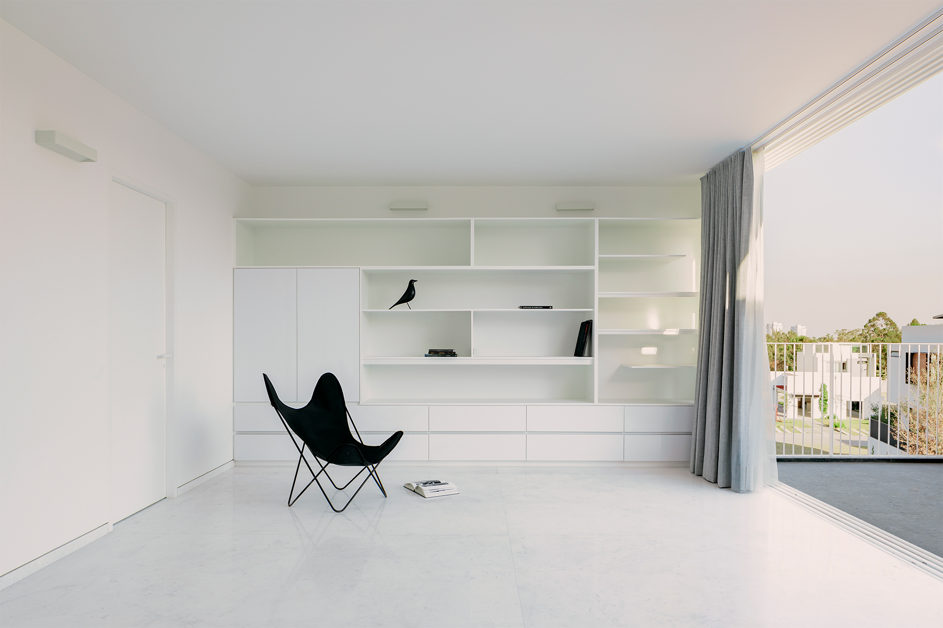 White interior with full-height built-in shelving and butterfly chair beside sliding glass doors