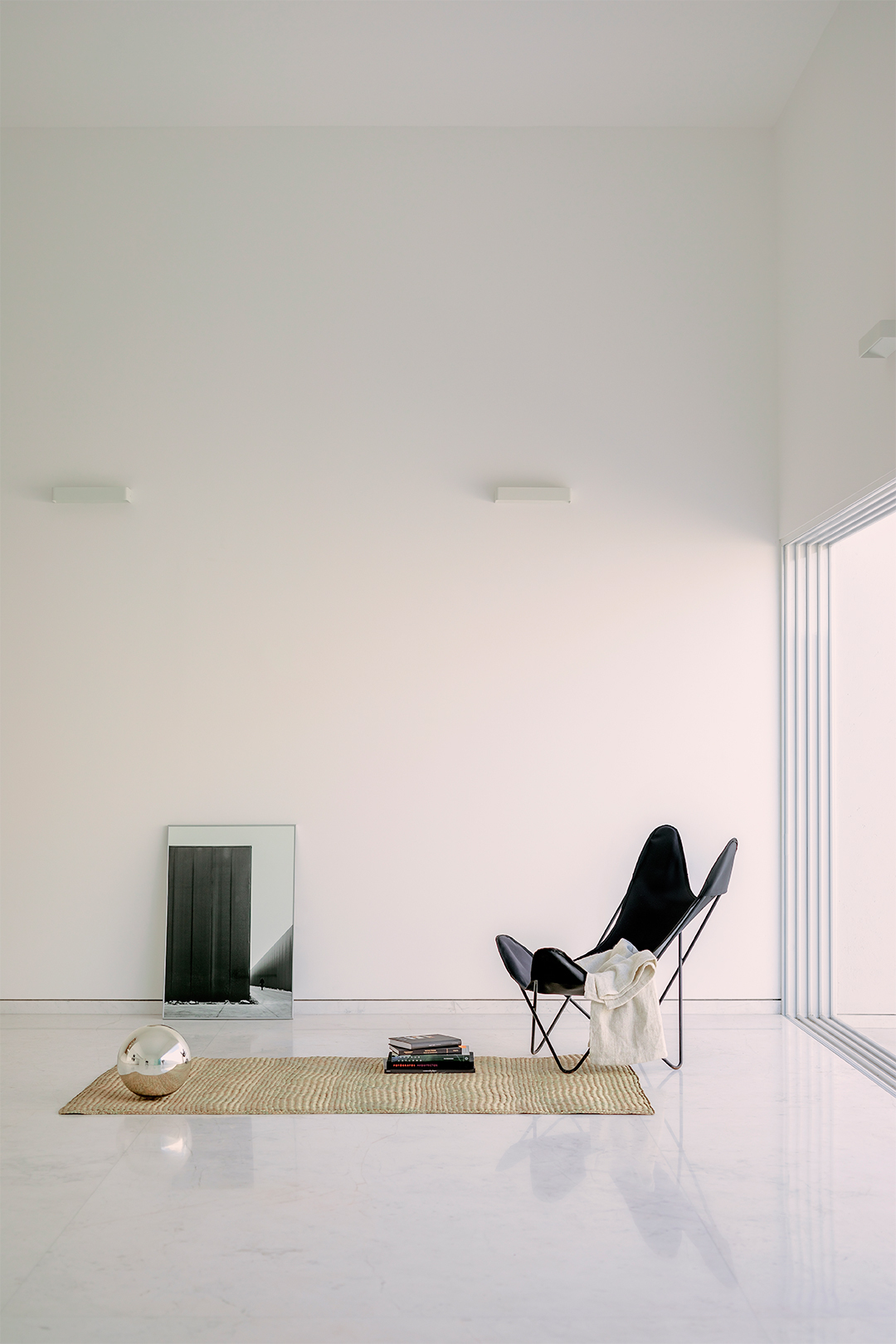 Sitting area with butterfly chair on woven rug beside floor-to-ceiling folding glass doors