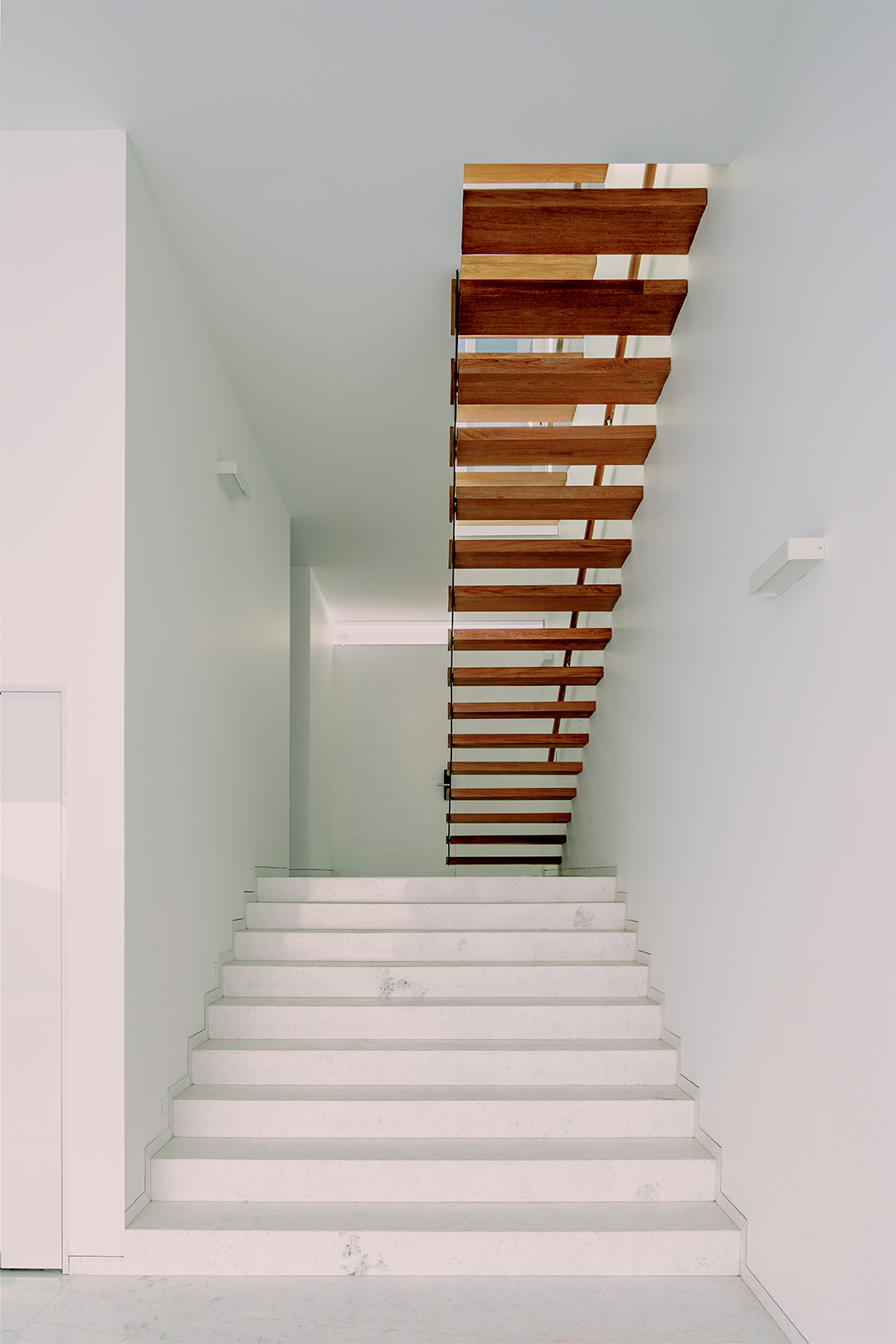 White terrazzo staircase with floating timber treads ascending through a double-height void