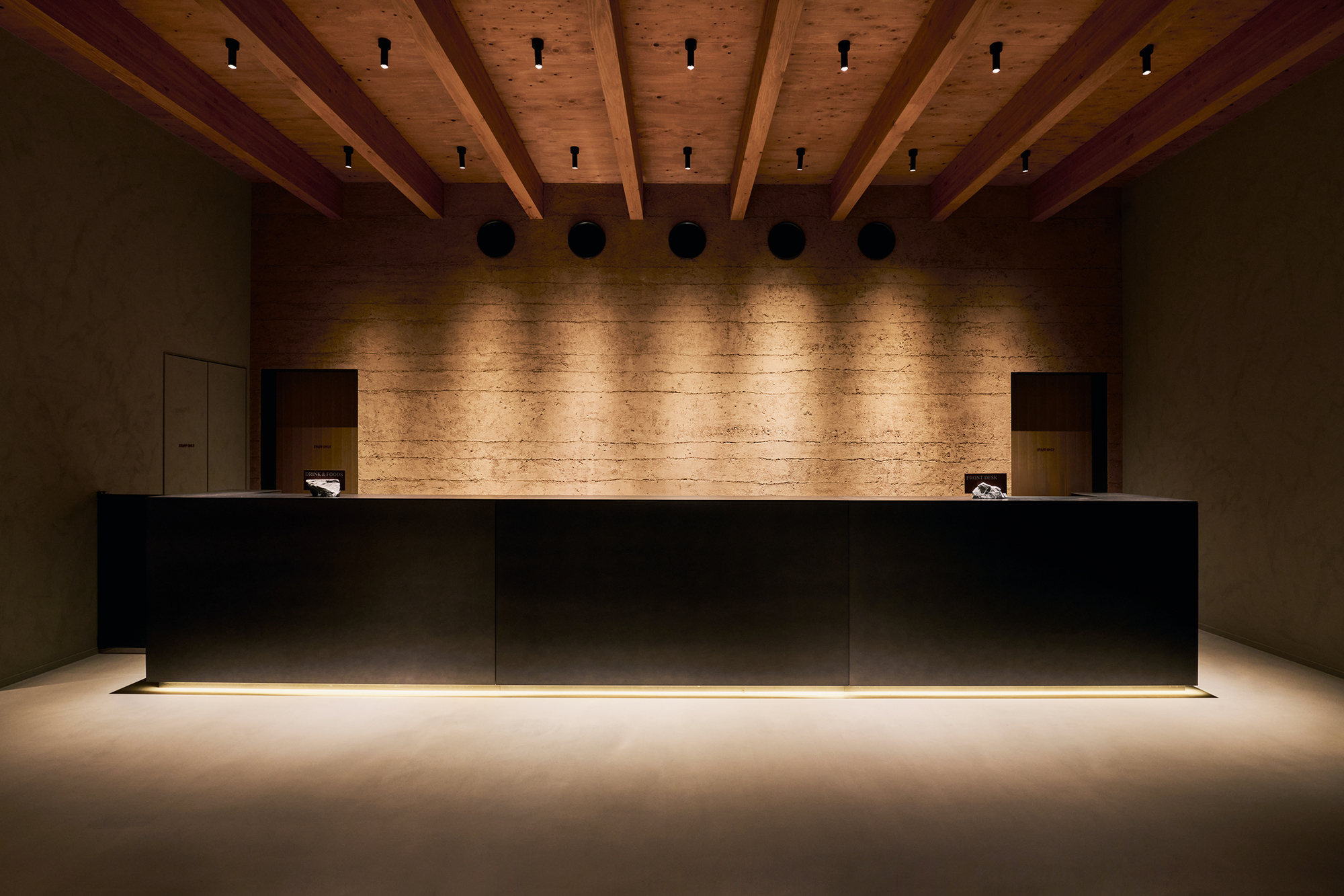 Reception desk with floating black volume and underlit base beneath exposed timber beams and downlights