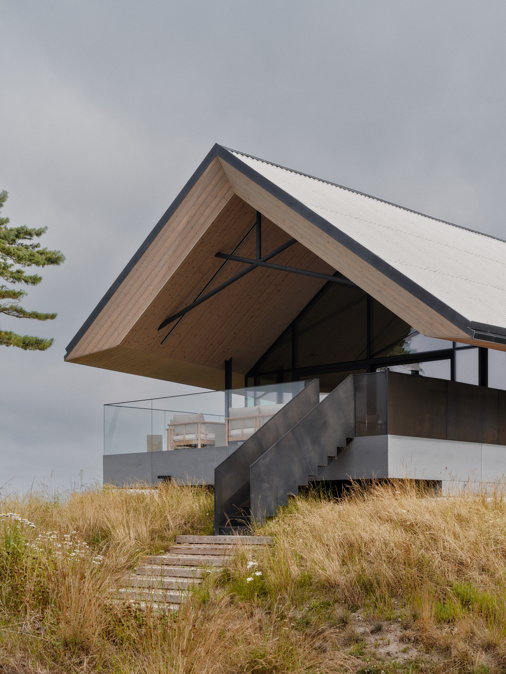 Cantilevered roof over concrete stair leading through dry coastal grasses under stormy skies