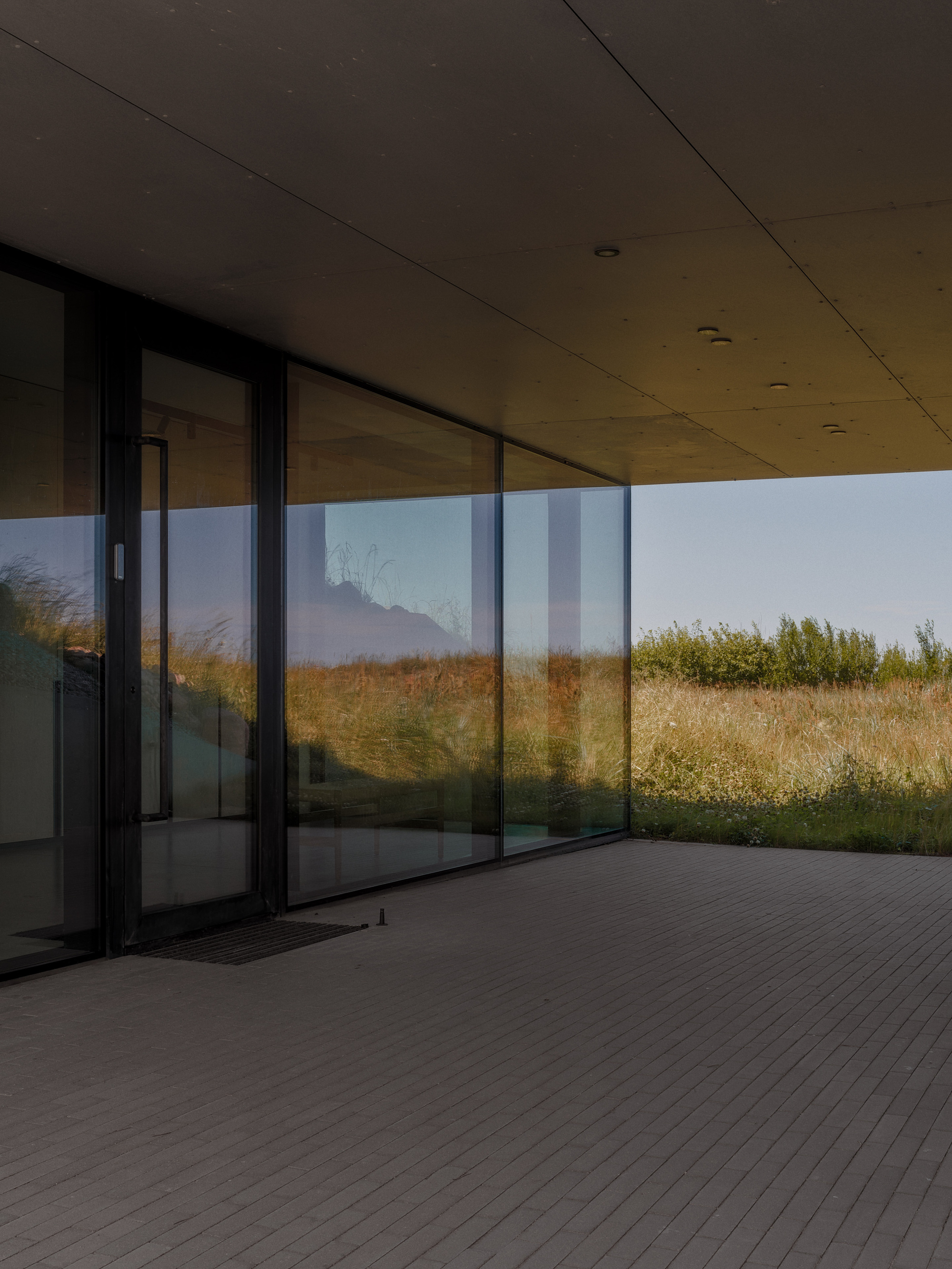 Covered timber deck with sliding glass doors opening to a grassy hillside at dusk