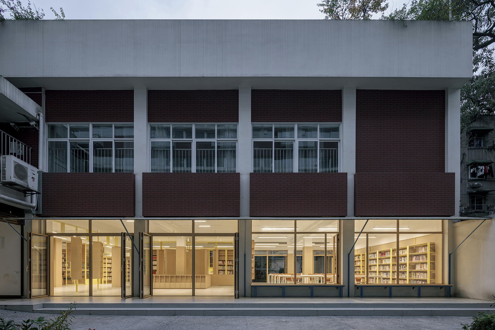 Street-facing facade with alternating bands of dark brick panels and full-height glazing at dusk