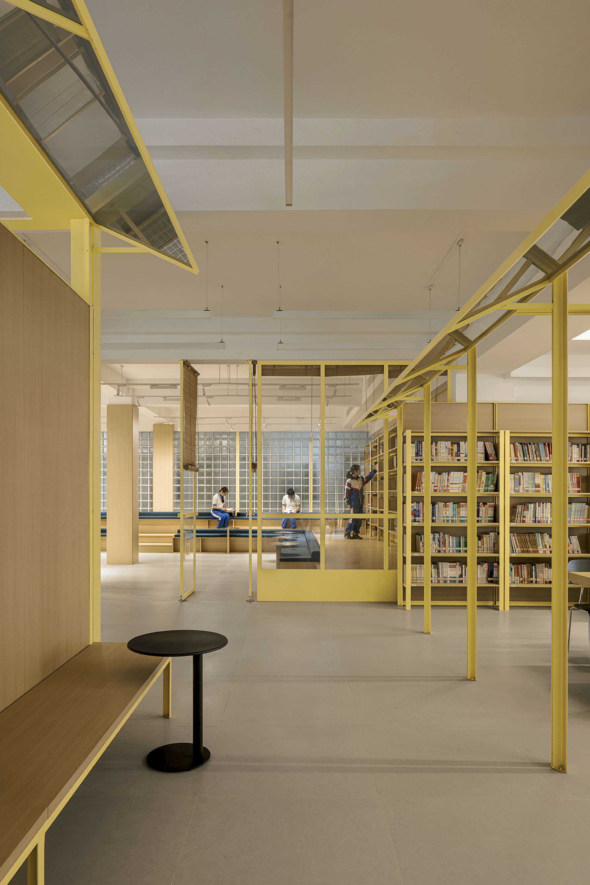 Reading area framed by yellow steel columns and beams with visitors seated on benches beneath pendant lights