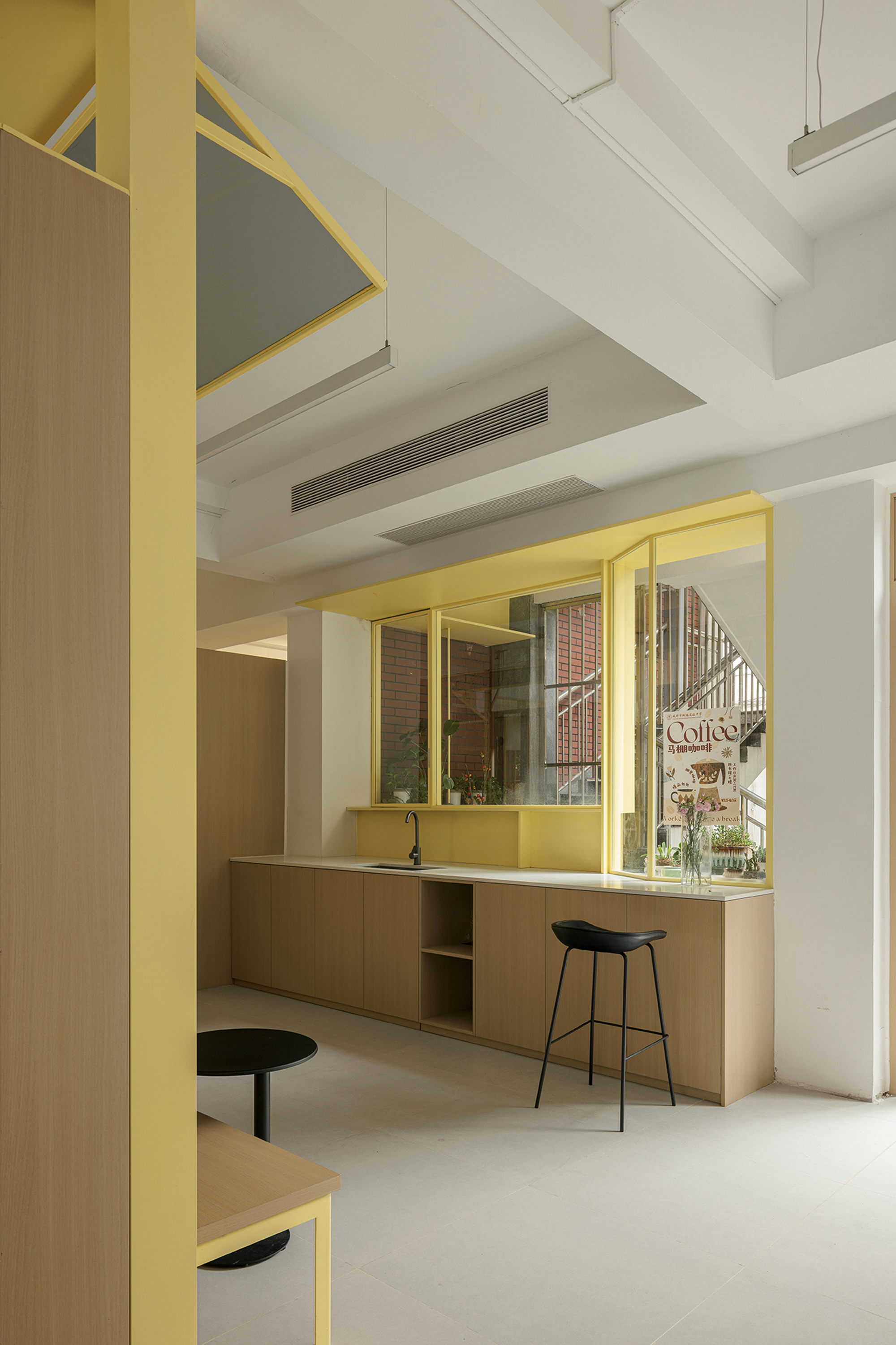 Service counter with timber cabinetry and black stools beneath a yellow steel framed opening with mirror
