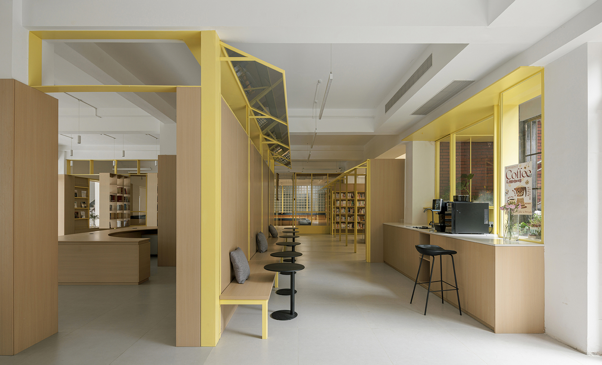 Long view through yellow steel frames organizing light timber counters and shelving in a bookshop interior