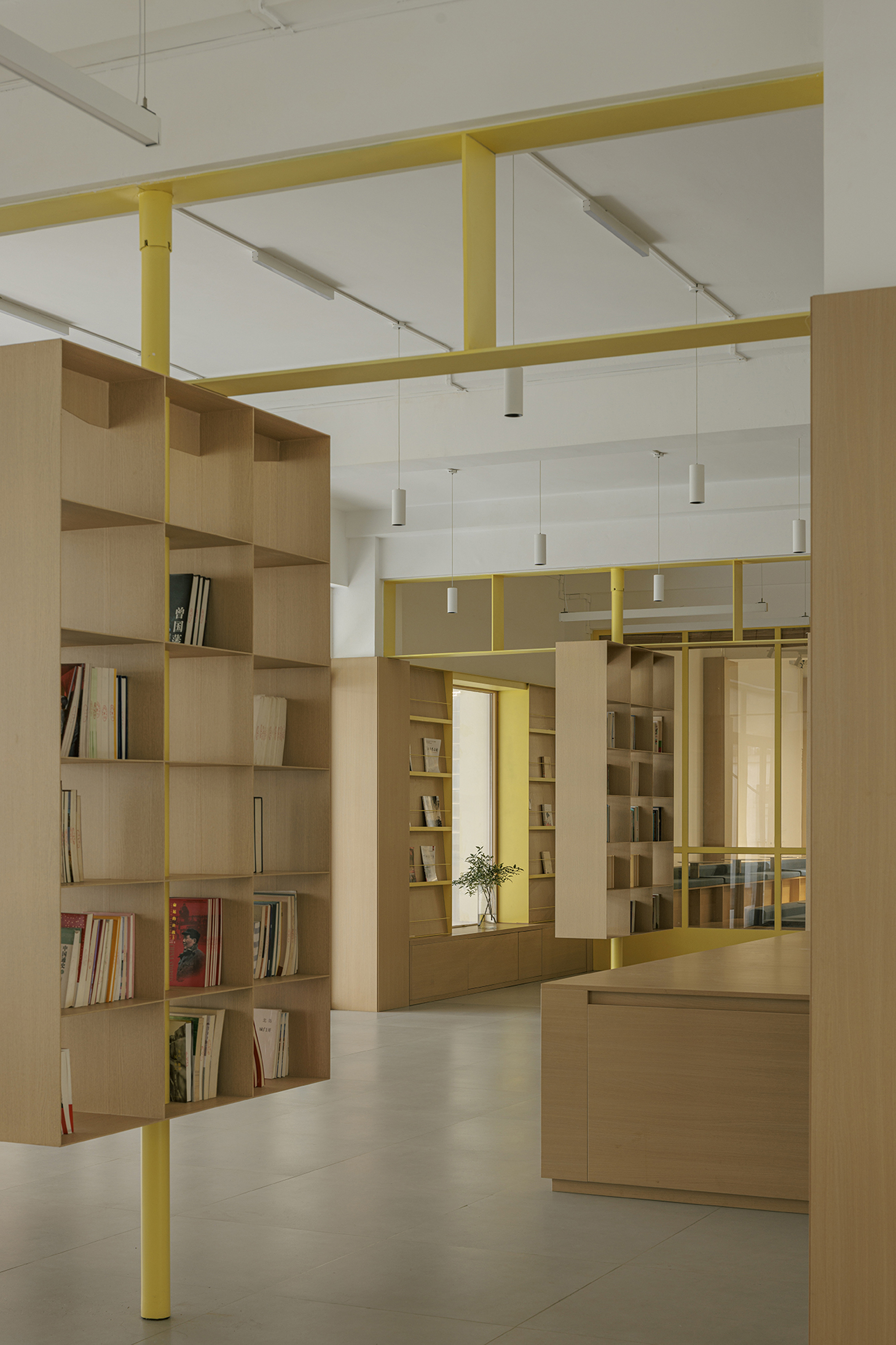 Light timber shelving units beneath yellow steel portal frames with cylindrical pendant fixtures overhead