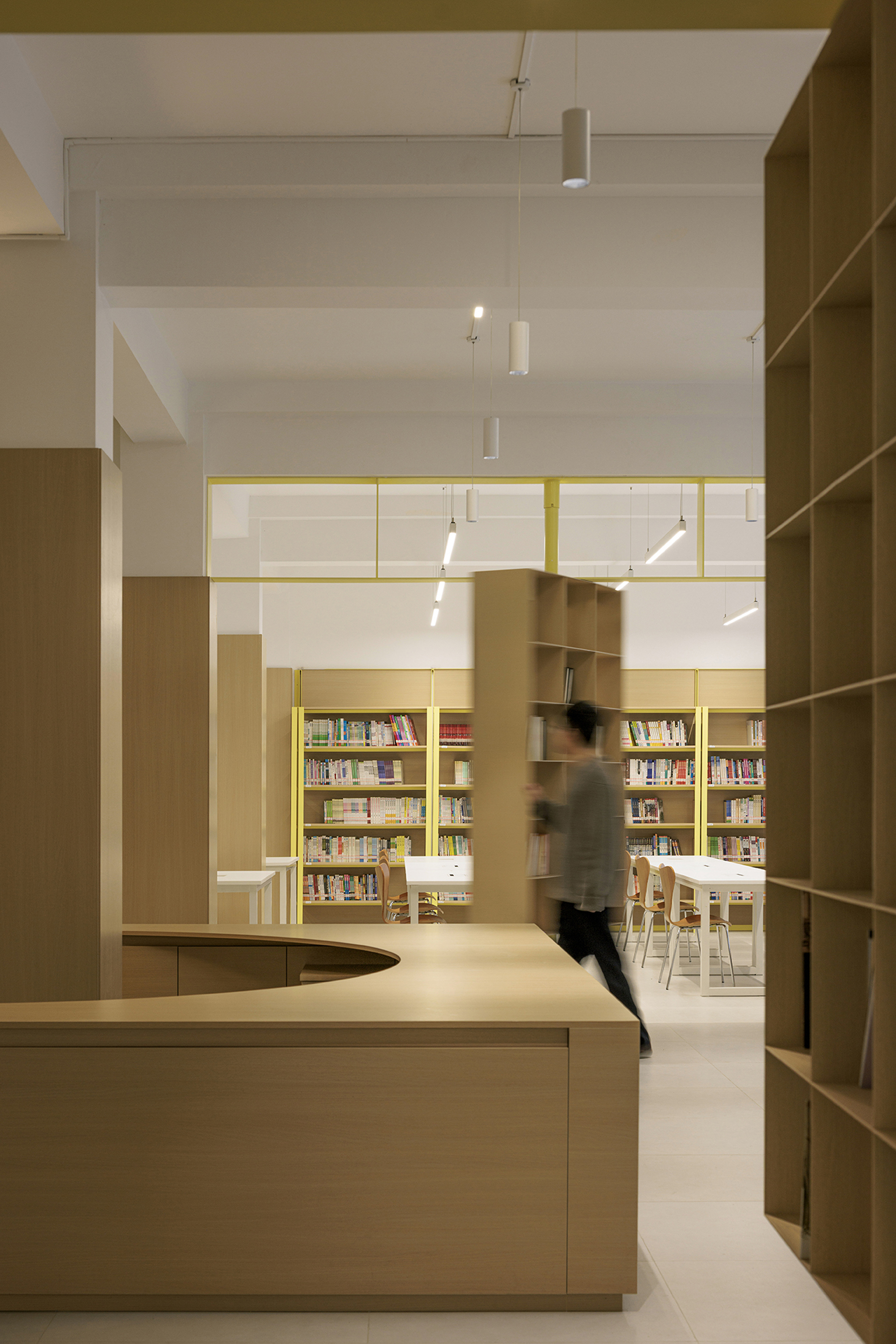Framed view through yellow steel portals toward a reading area with a figure in motion