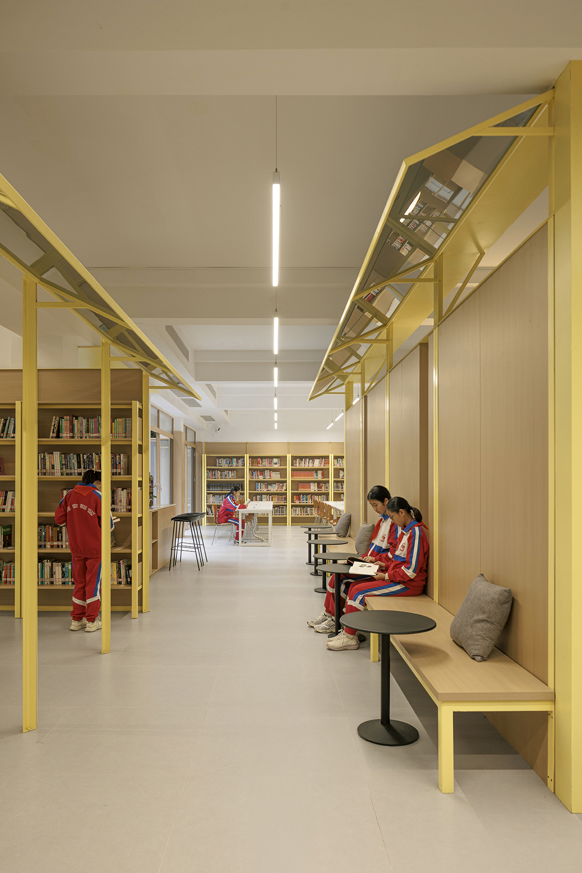 Library corridor with yellow steel structural frames and seated readers in red uniforms