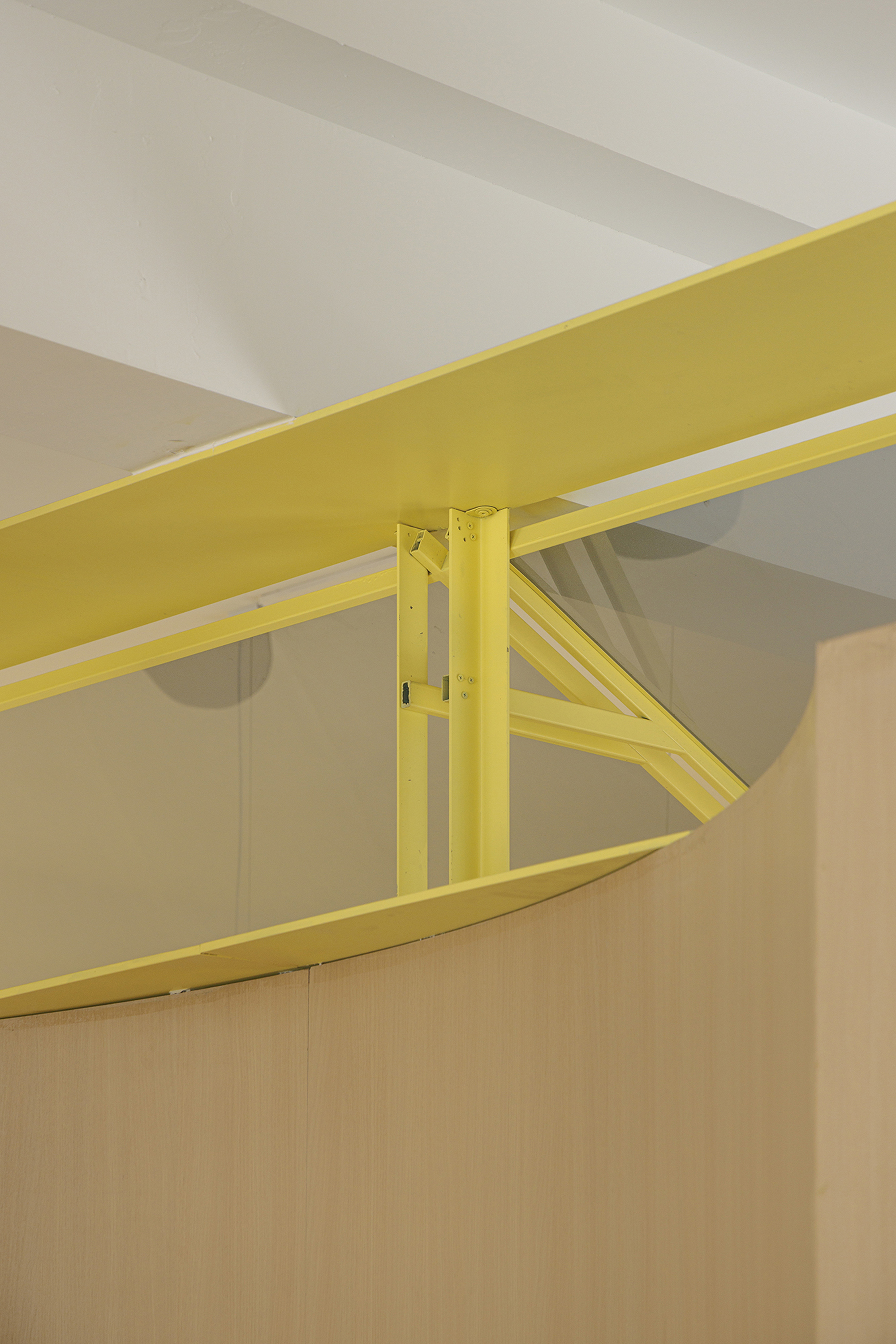 Close-up of yellow steel beam connection with diagonal bracing against white ceiling