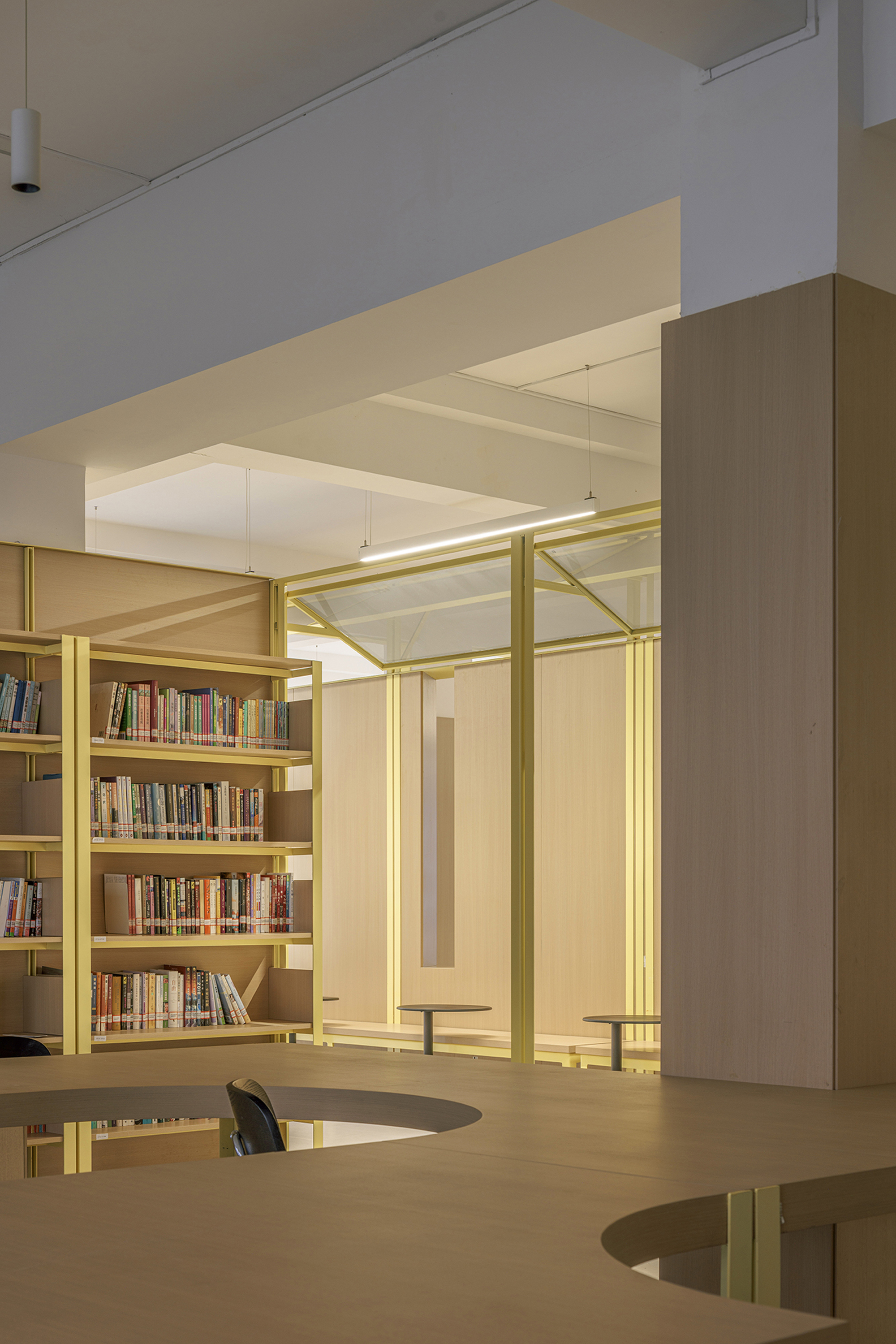 View through yellow steel columns toward bookshelves and glazed opening with evening light