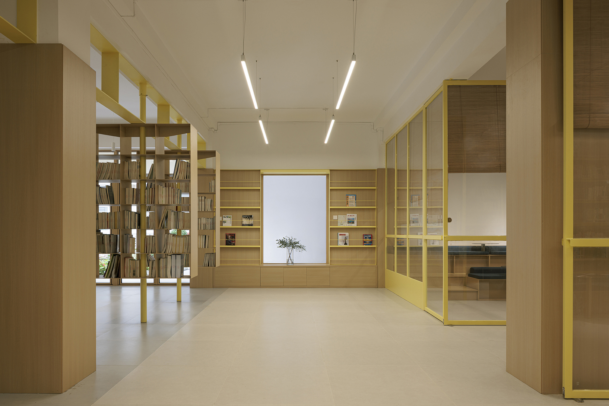 Library interior with yellow metal frame shelving and timber cabinetry under linear ceiling lights