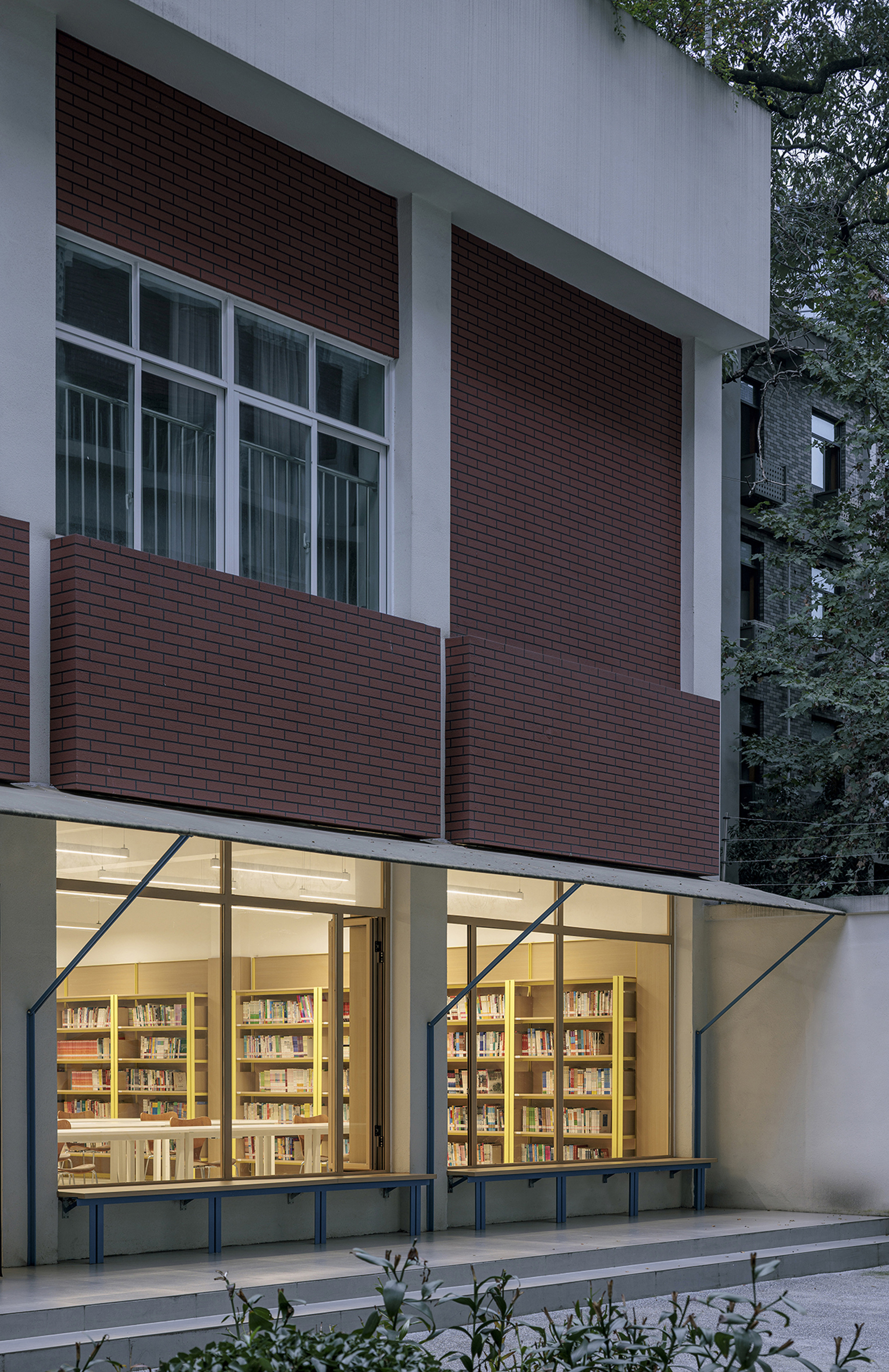 Facade detail showing maroon brick panels and illuminated ground floor windows at dusk