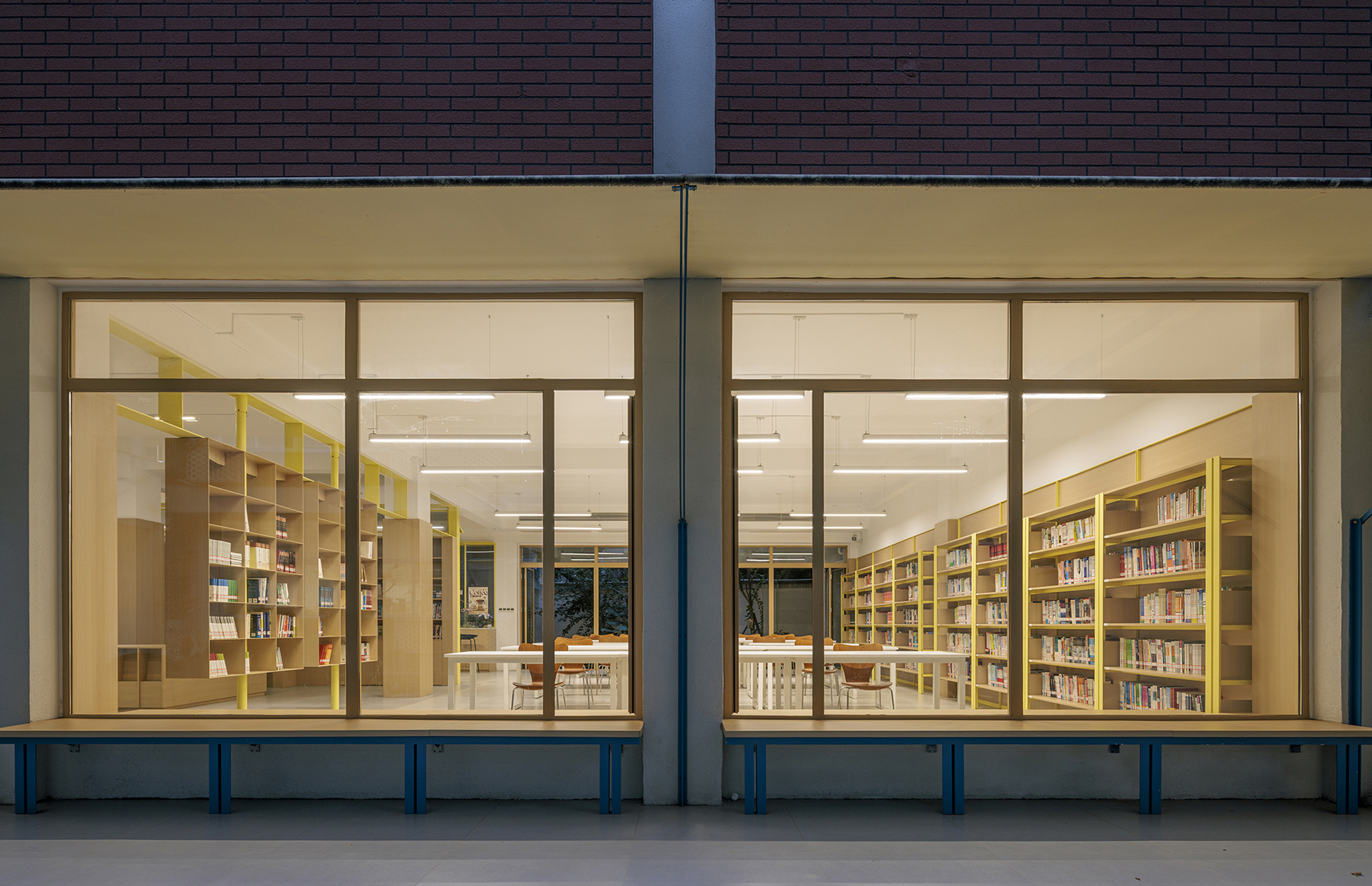 Storefront glazing revealing library shelves and reading tables under evening light