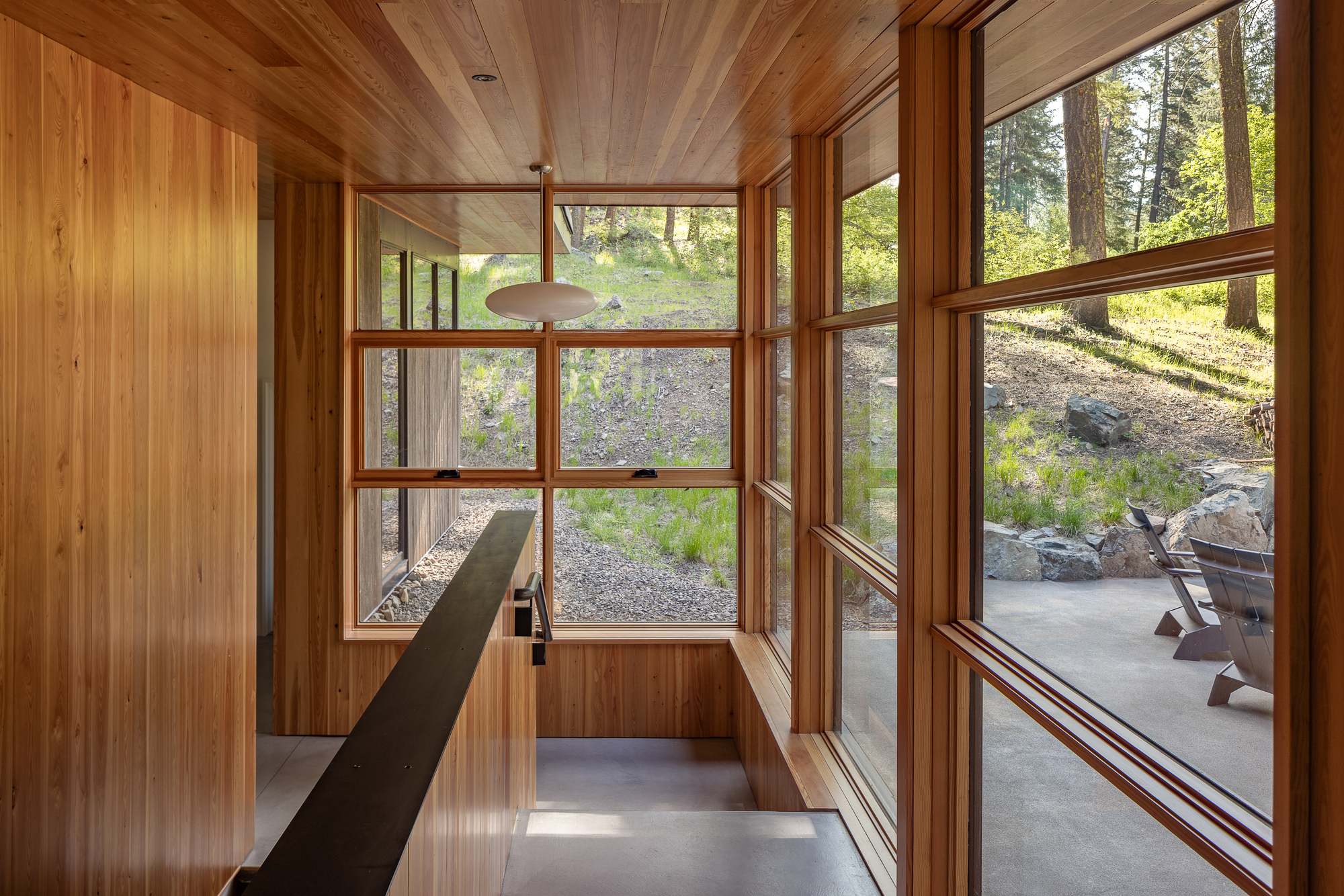 Glass-walled hallway with timber cladding leading to an outdoor patio and gravel landscape
