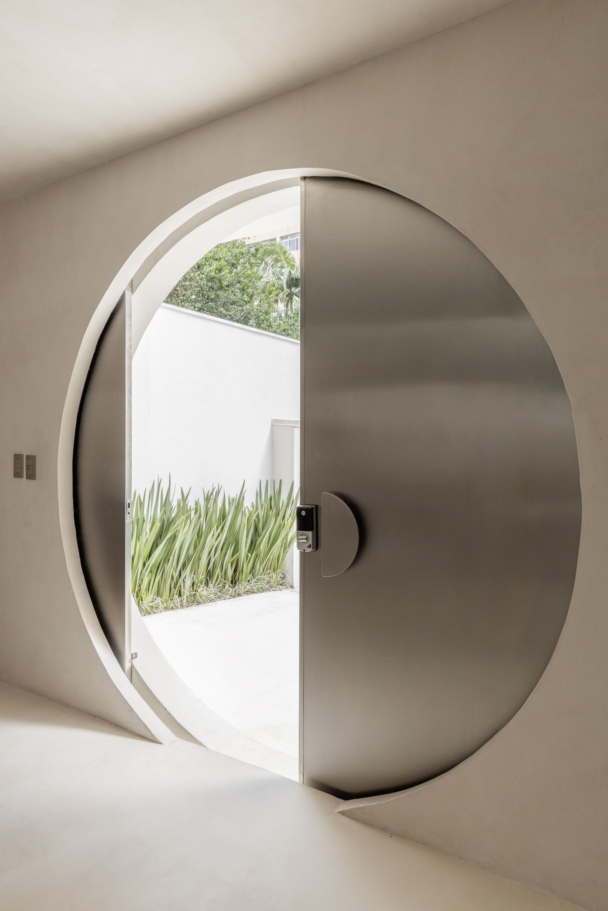 Circular pivot door with stainless steel panel opening to a planted courtyard with grasses