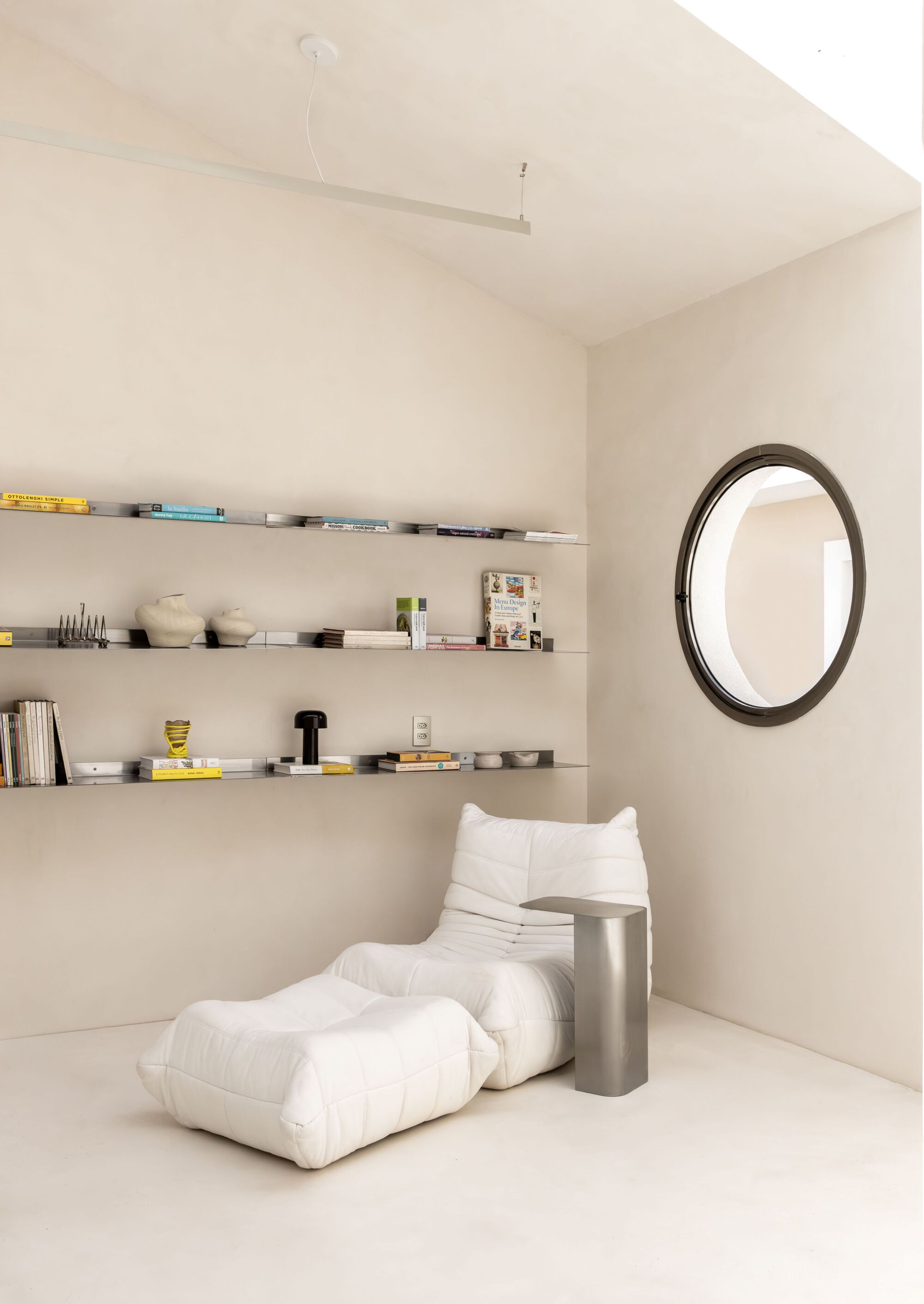 Corner nook with floating shelves and white lounge seating beneath a vaulted ceiling