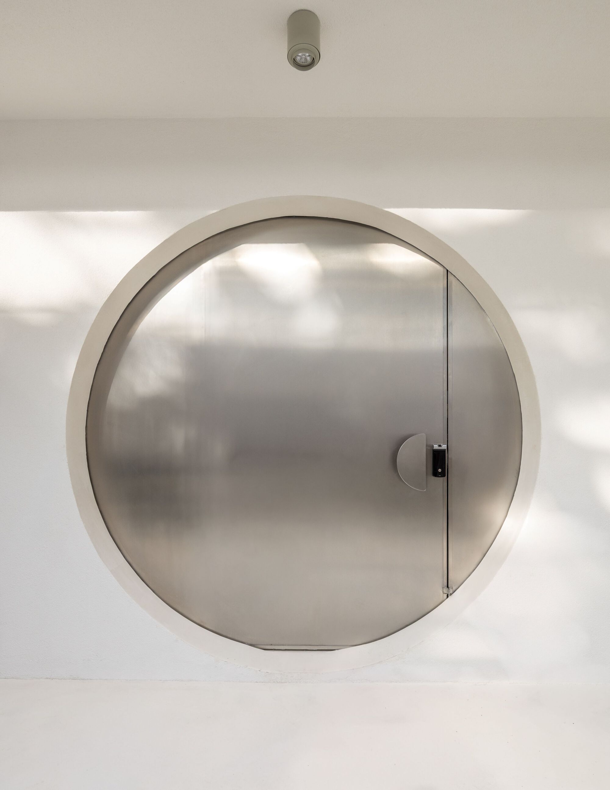 Closed circular stainless steel door set within white plastered wall