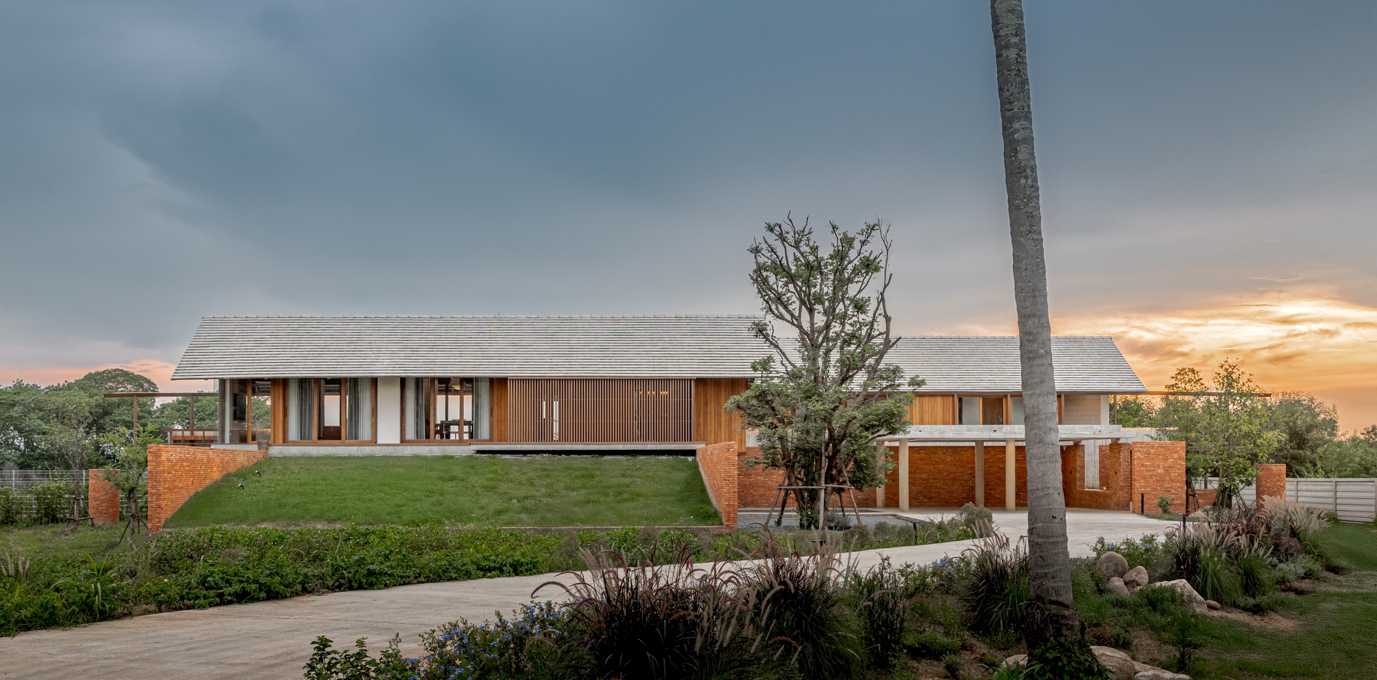 Entry facade with timber shutters and brick base flanked by palm trees at sunset
