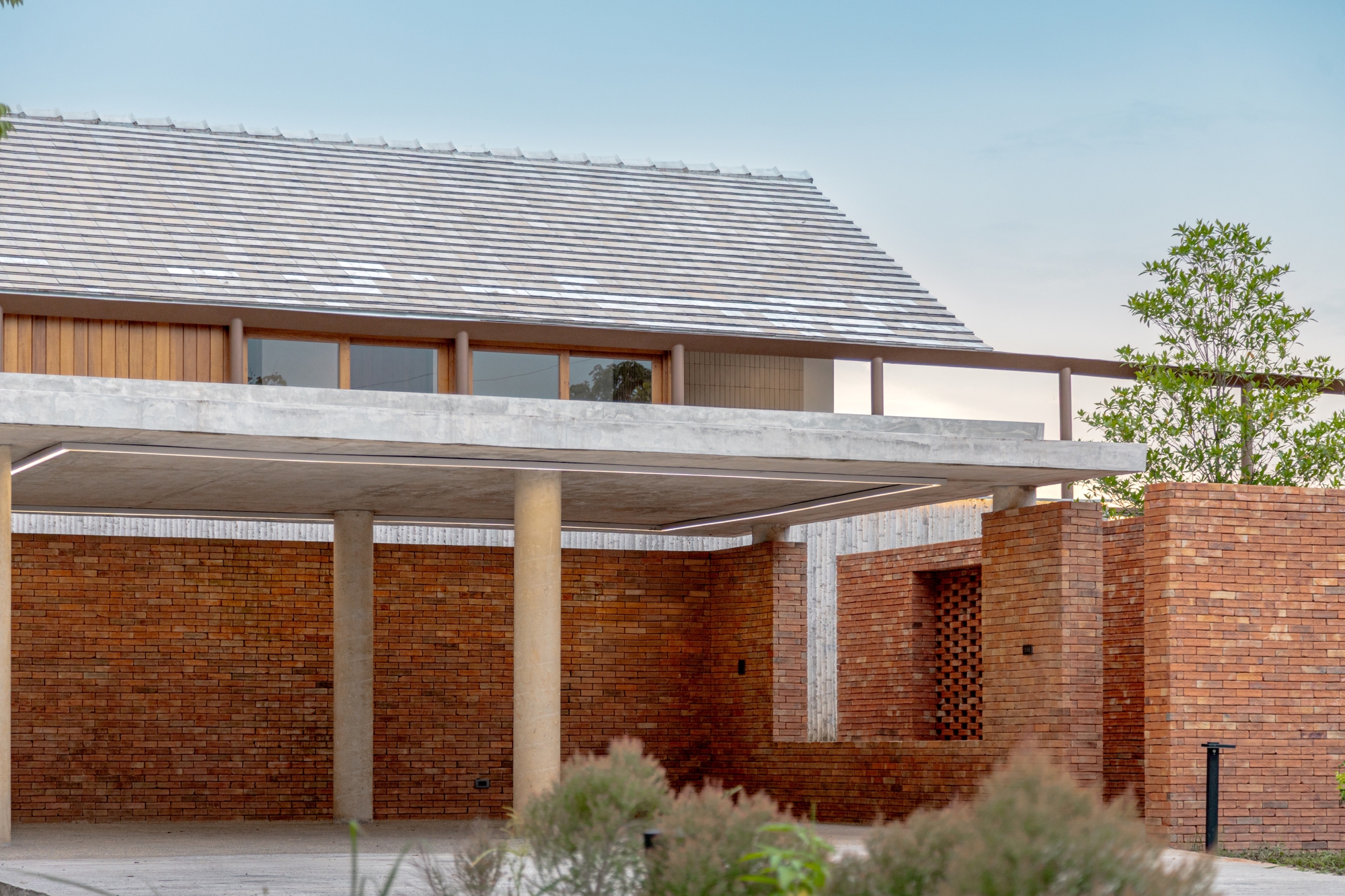 Covered carport with cylindrical concrete columns supporting a broad roof slab above brick walls