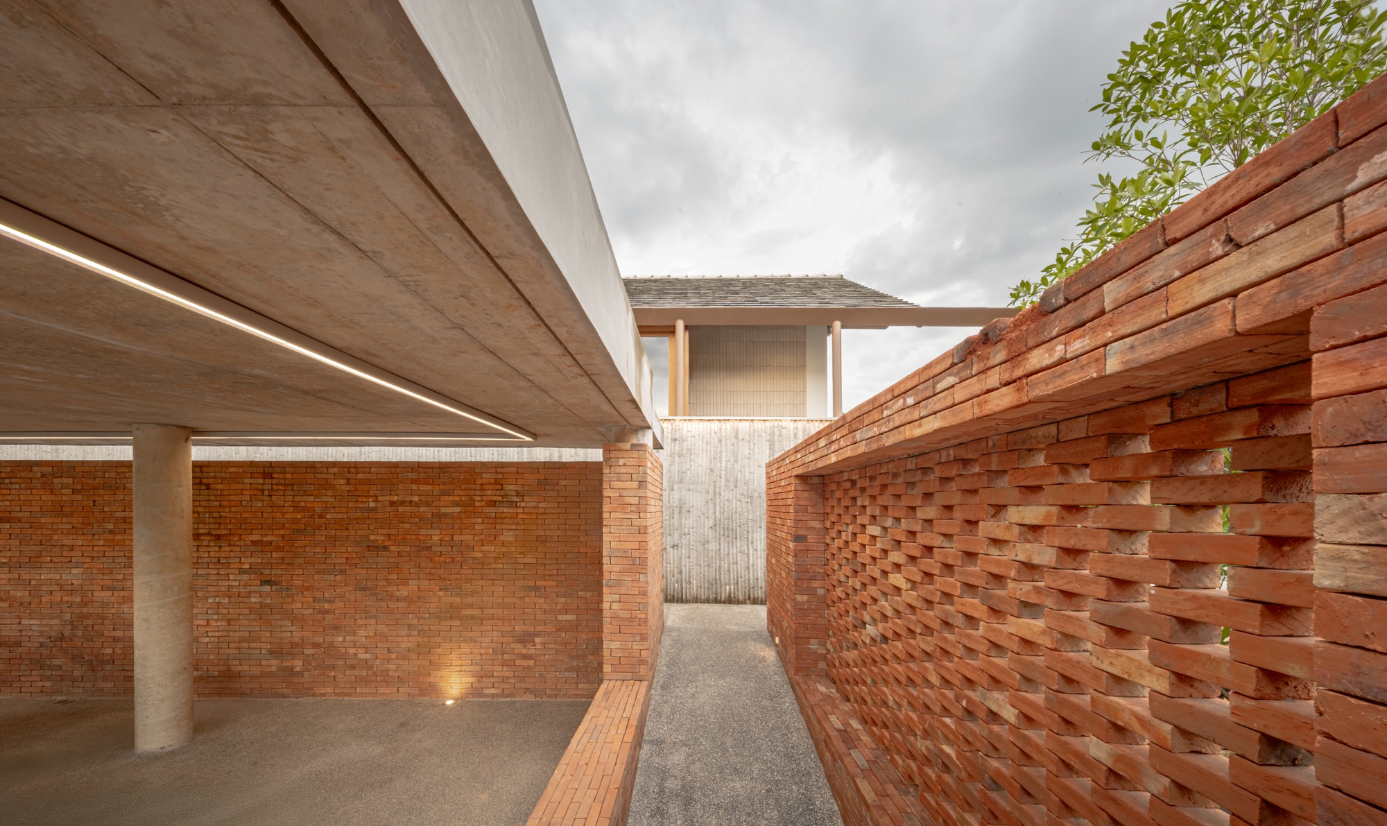 Narrow courtyard passage framed by perforated brick walls and a concrete soffit with linear lighting